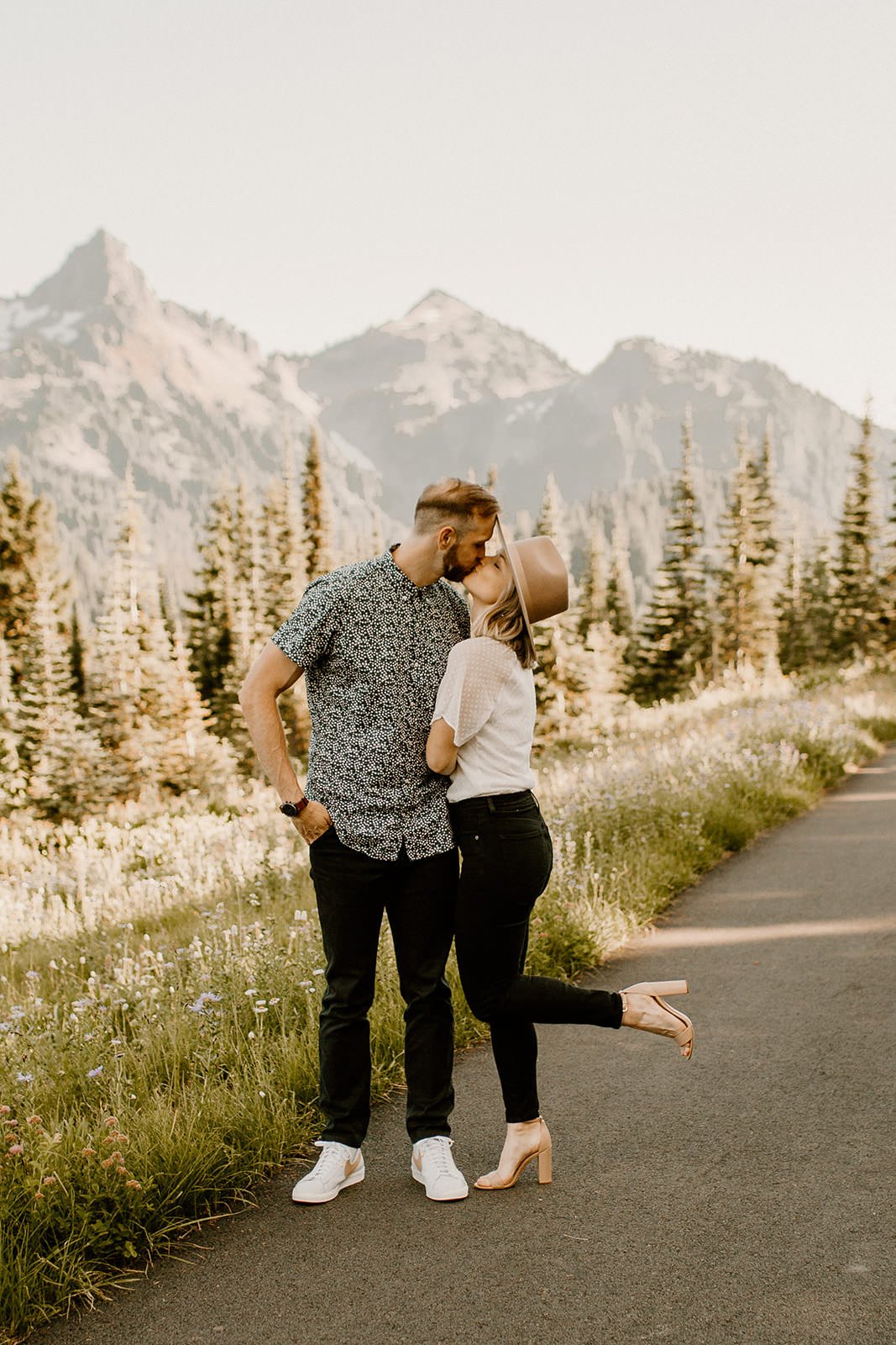 couple kissing in mt. rainier national park, girl has foot kicked up and mountains are in the background
