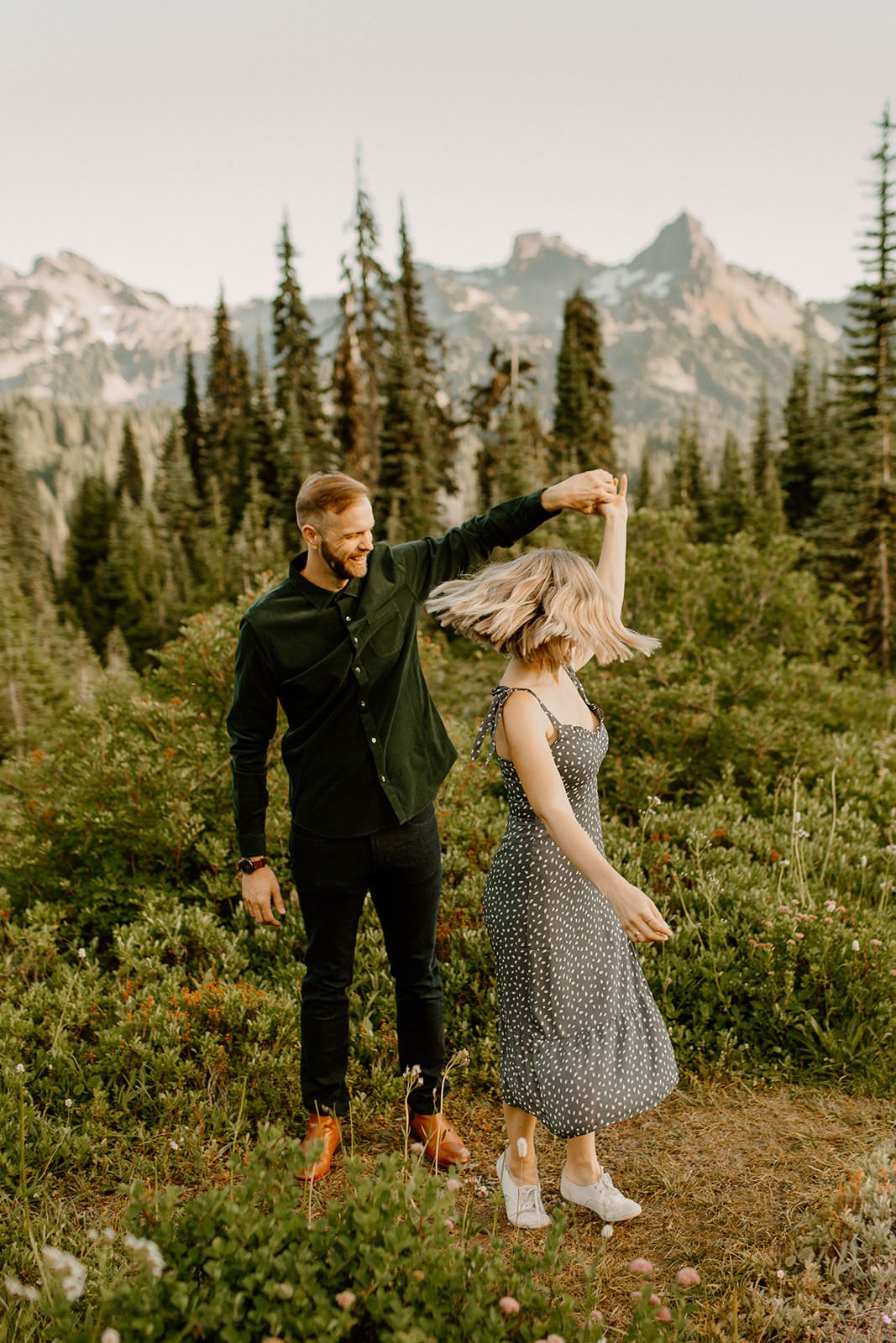 fiance twirling his partner in a meadow with mountains in the background