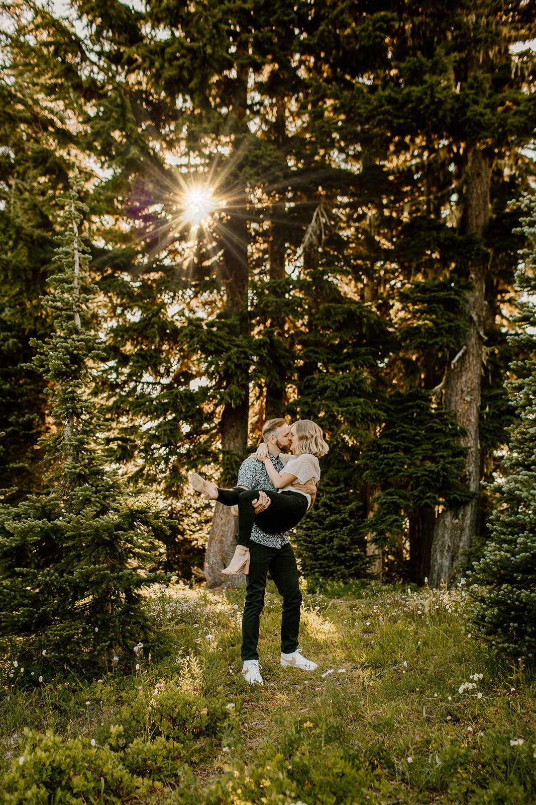 fiance picking his partner up and kissing her in the trees at mt. rainier national park