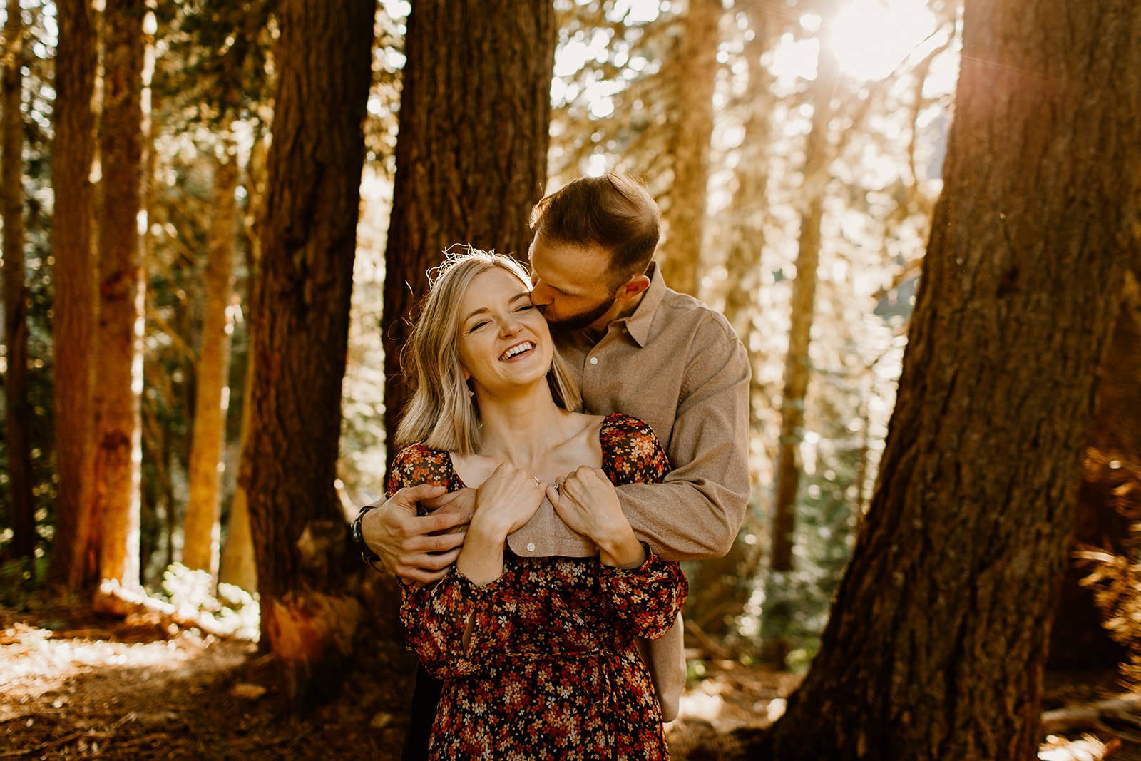 golden hour image of couple in the forest with fiance kissing his girlfriends cheek