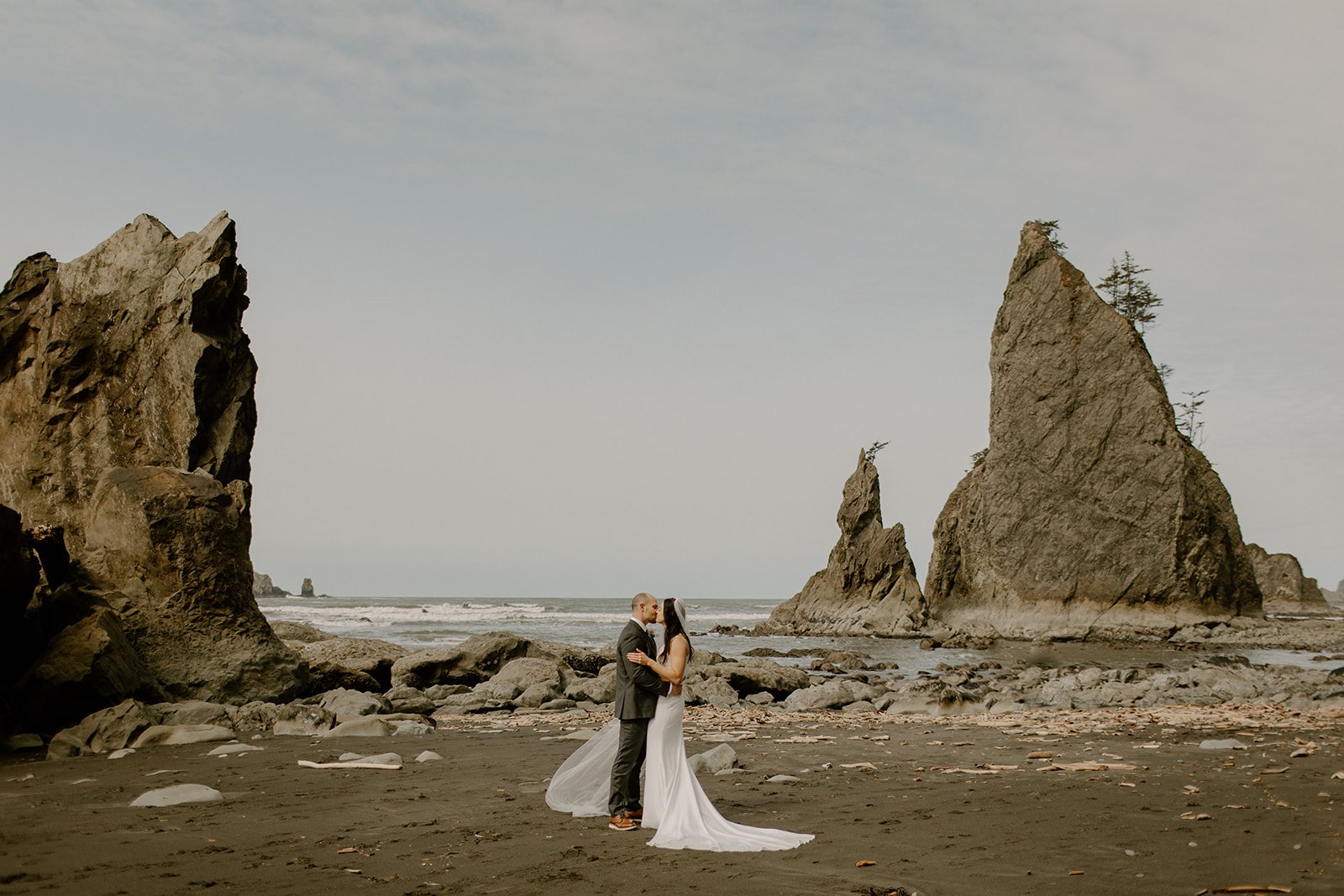 bride and groom kissing on ruby beach in washington in between sea haystacks