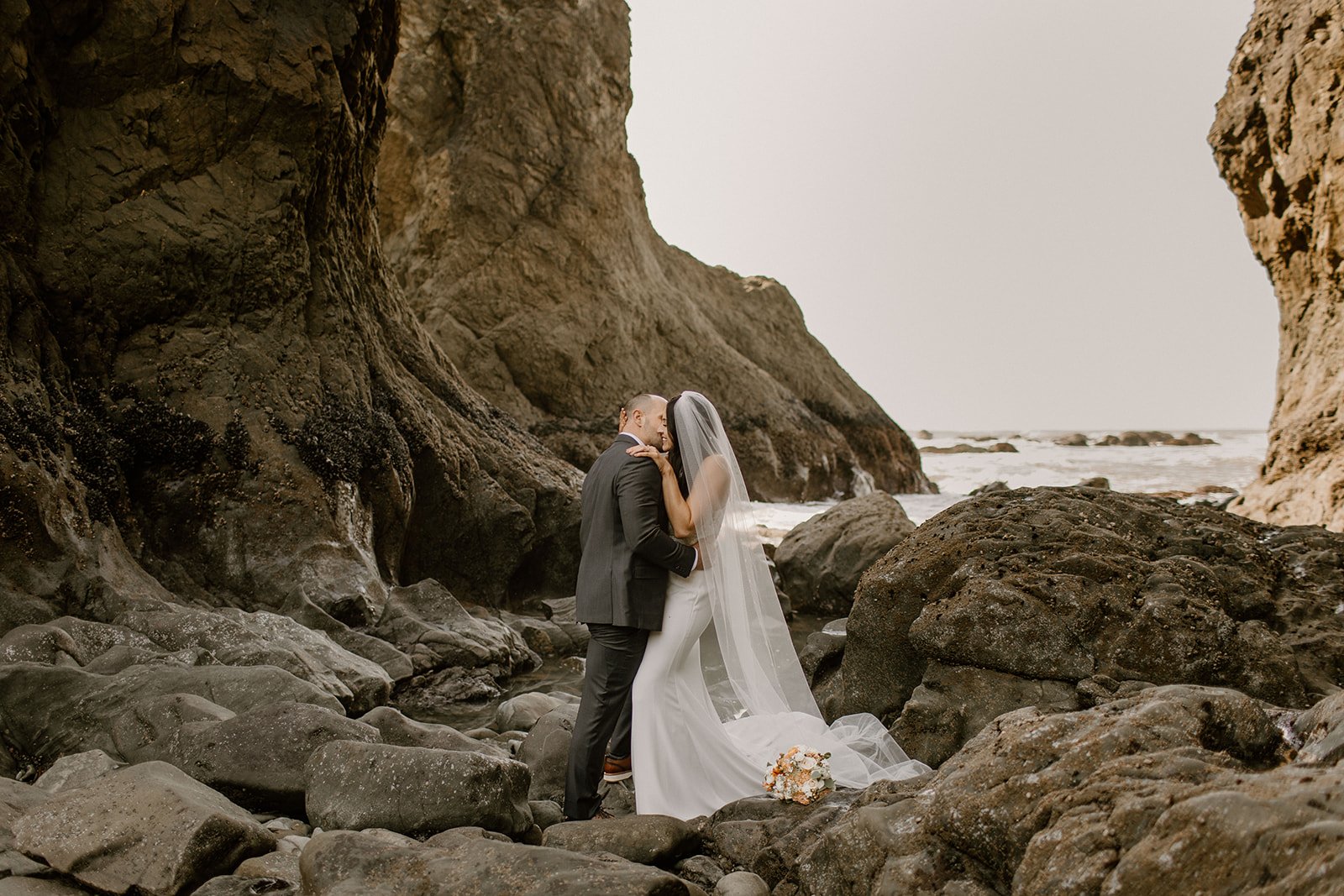Bride and groom hugging on rocks and in front of cliffs on ruby beach in washington state