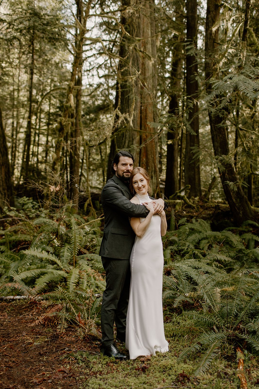 Groom hugging bride from behind in a forest in Olympic National Park
