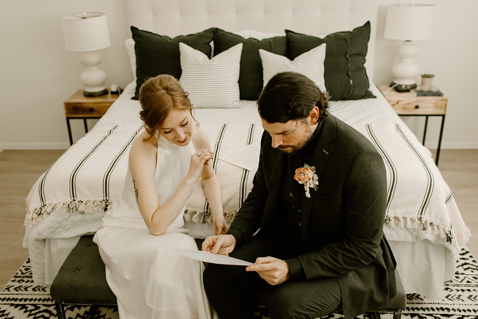 Groom reading a letter from his parents while seated next to the bride in the bedroom of their Airbnb