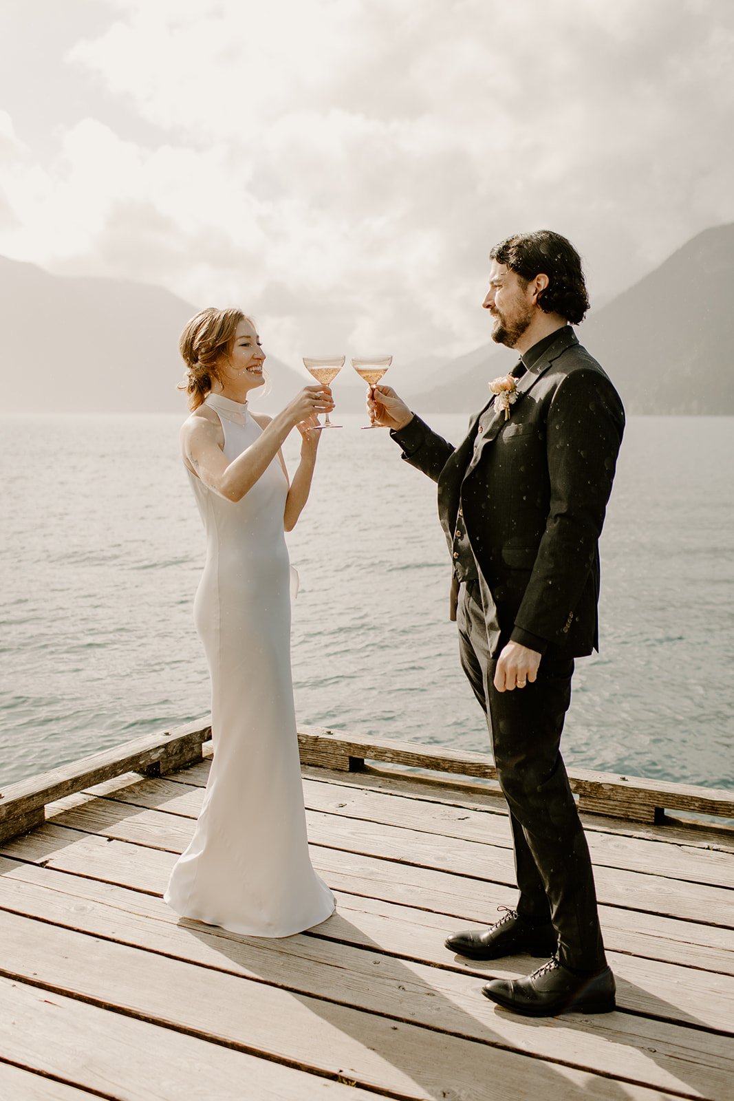 Bride and Groom standing on dock at lake crescent cheering with a glass of champagne