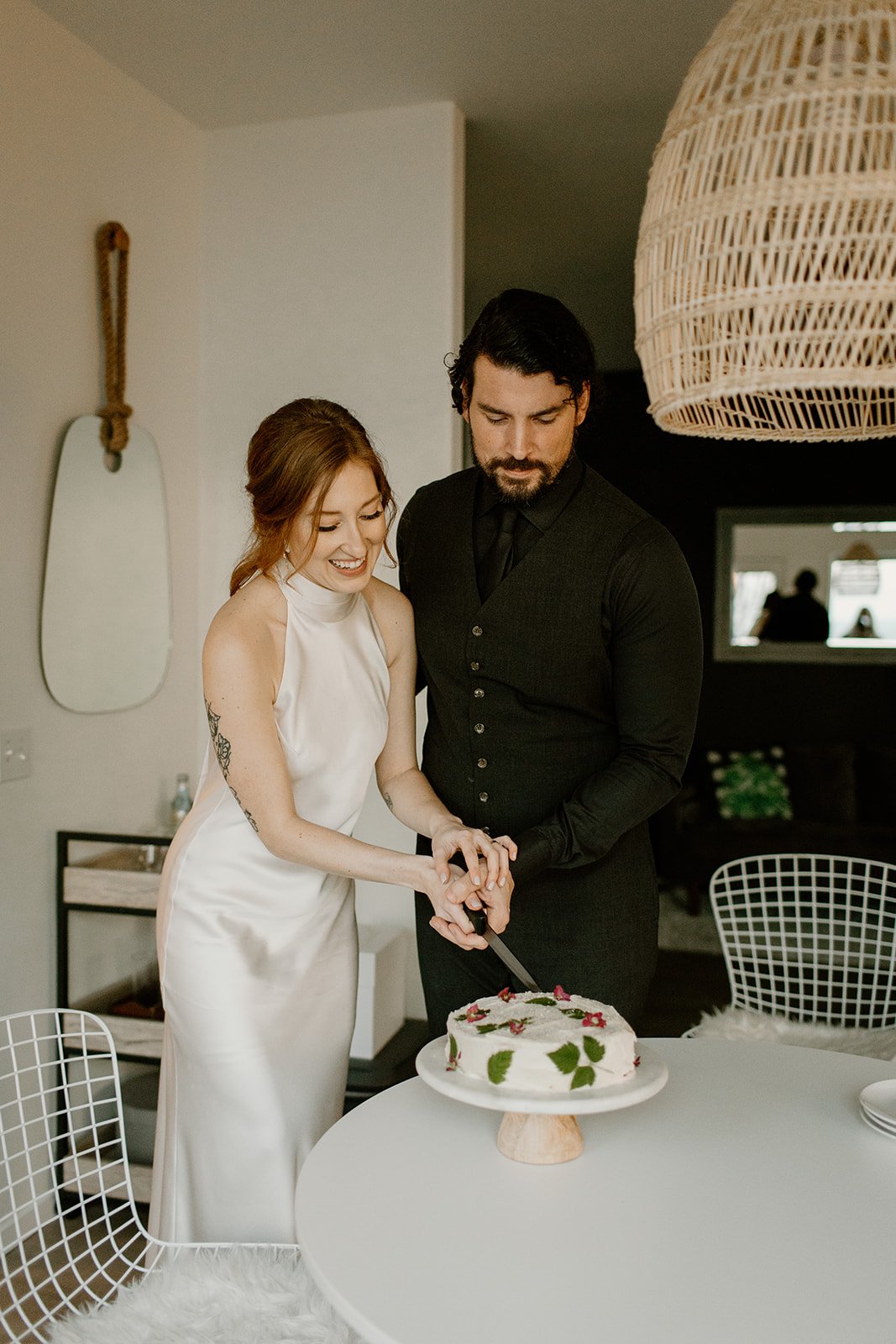 Bride and Groom in their wedding attire cutting their wedding cake inside the kitchen of their Airbnb