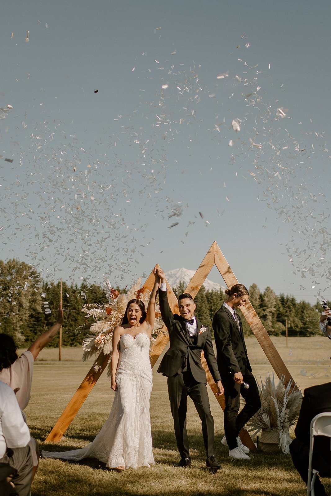 bride and groom raising their hands in celebration and walking down the aisle as confetti rains down on them