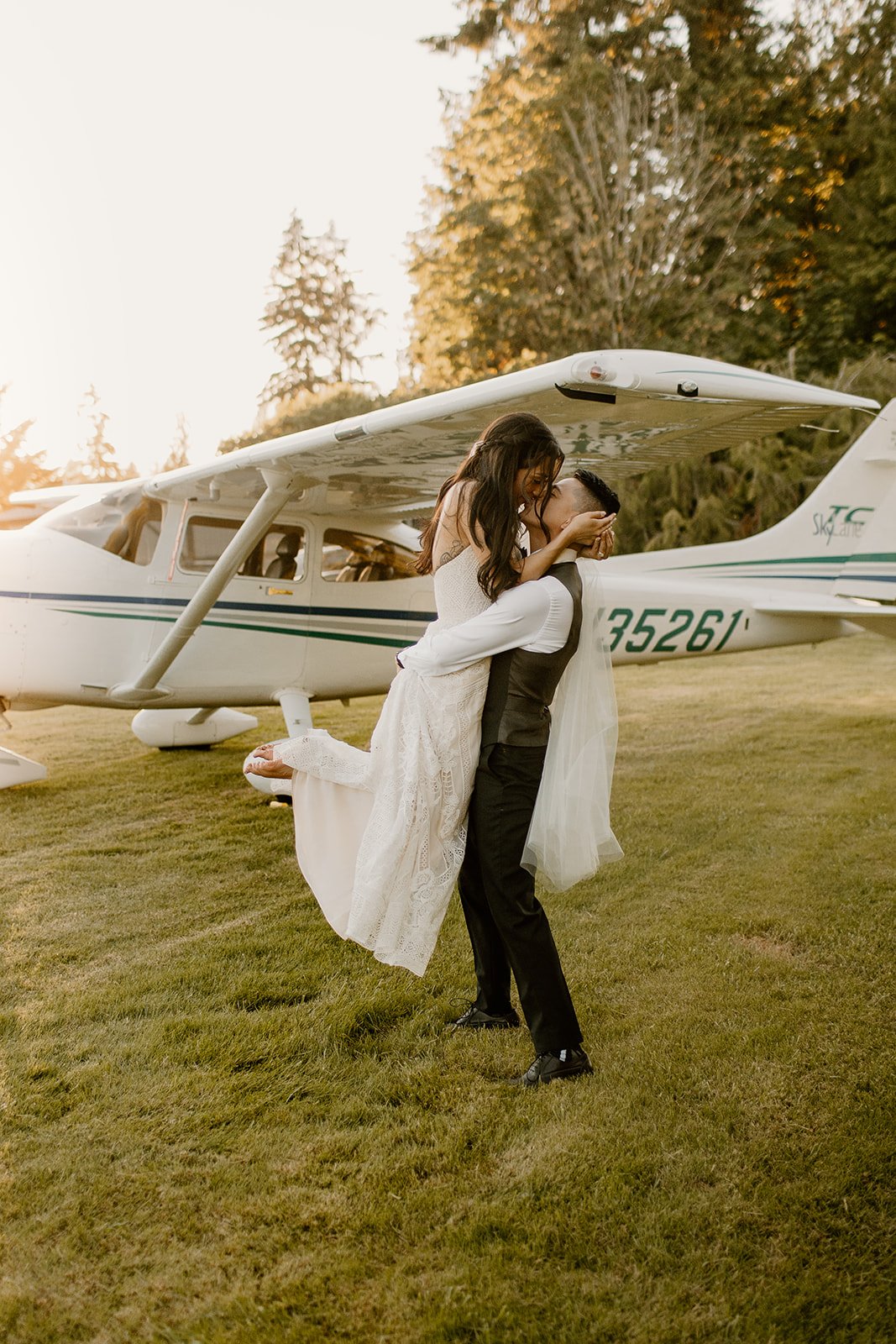 groom picking up the bride and kissing her at sunset in front of a hangar plane