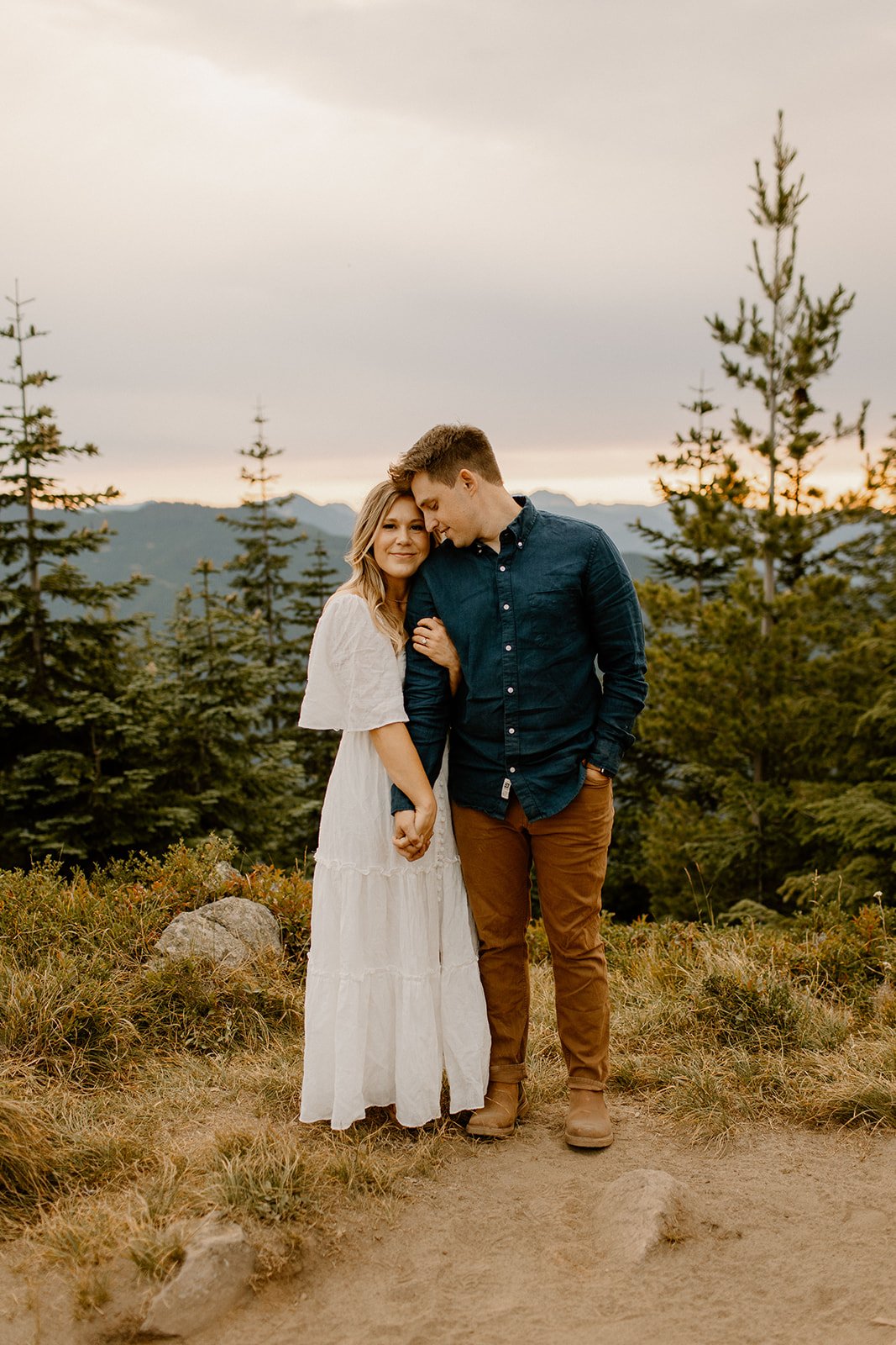 girl holding her fiance arm while looking and smiling at the camera during their engagment photos in mt rainier