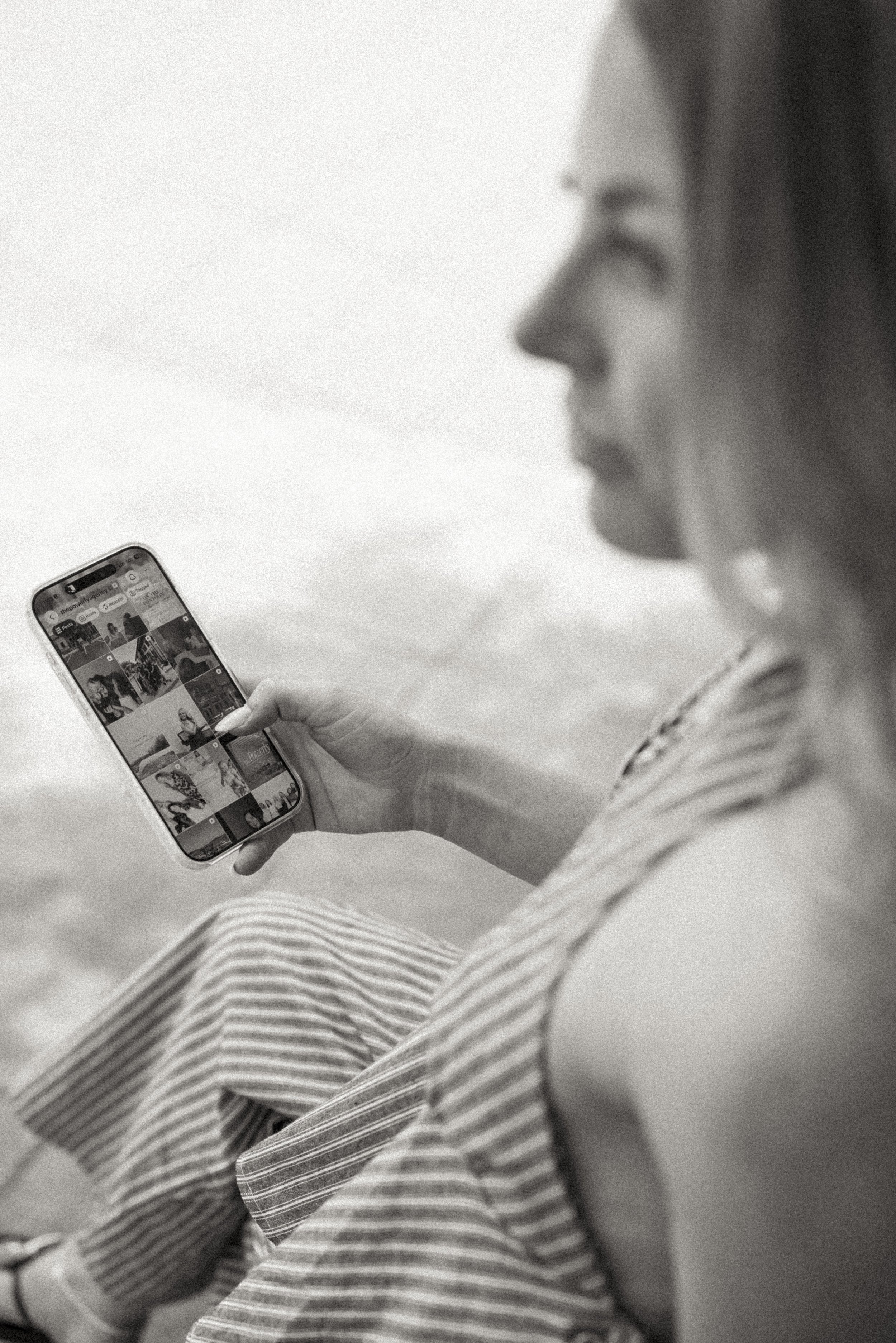 A woman in a striped shirt holding a smartphone, viewing a grid of photos on the screen, for a branding session in Greenville, SC by Melissa Glynn Photography