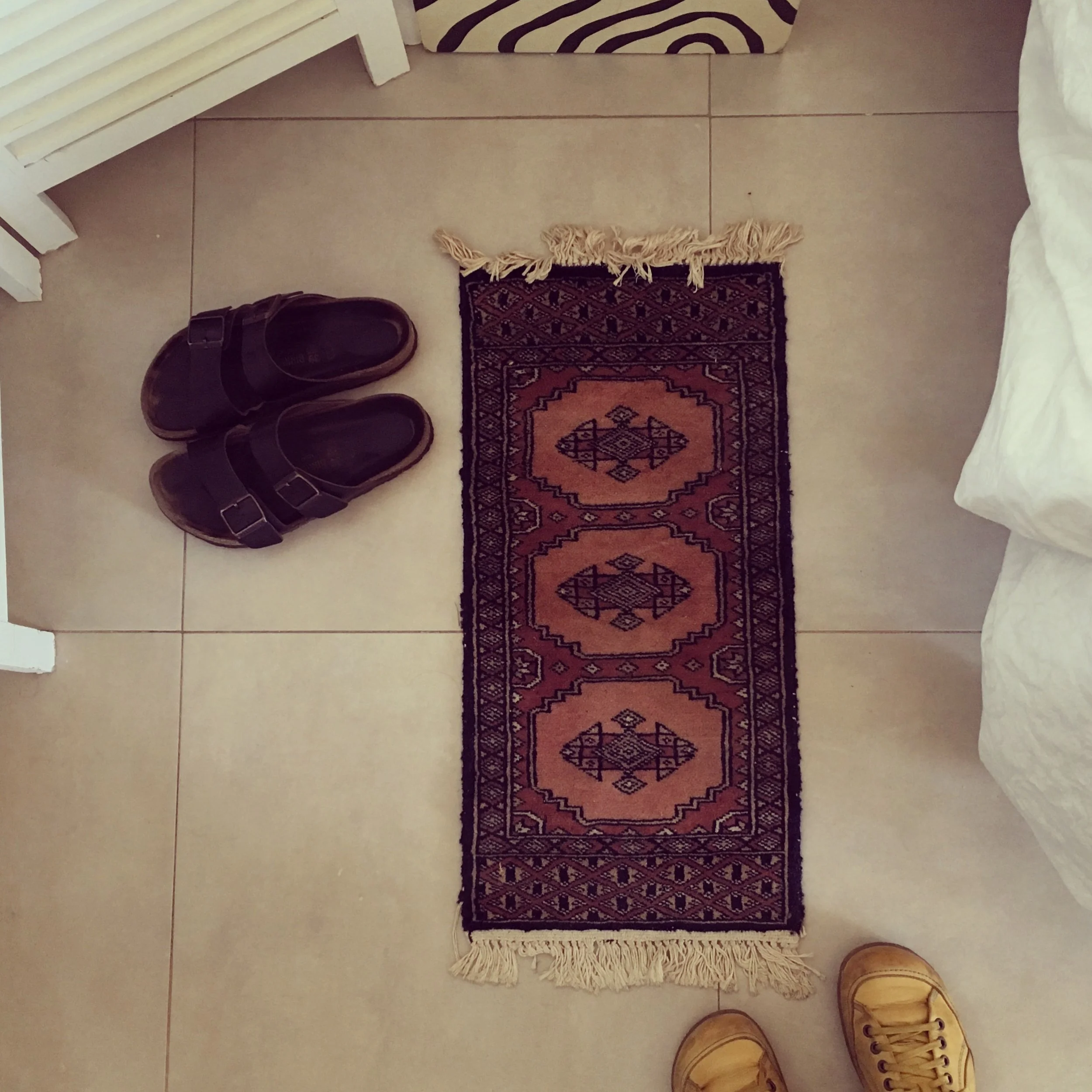 The rug, my sandals, and me in my travelling shoes across from the water in Sitges, Spain.