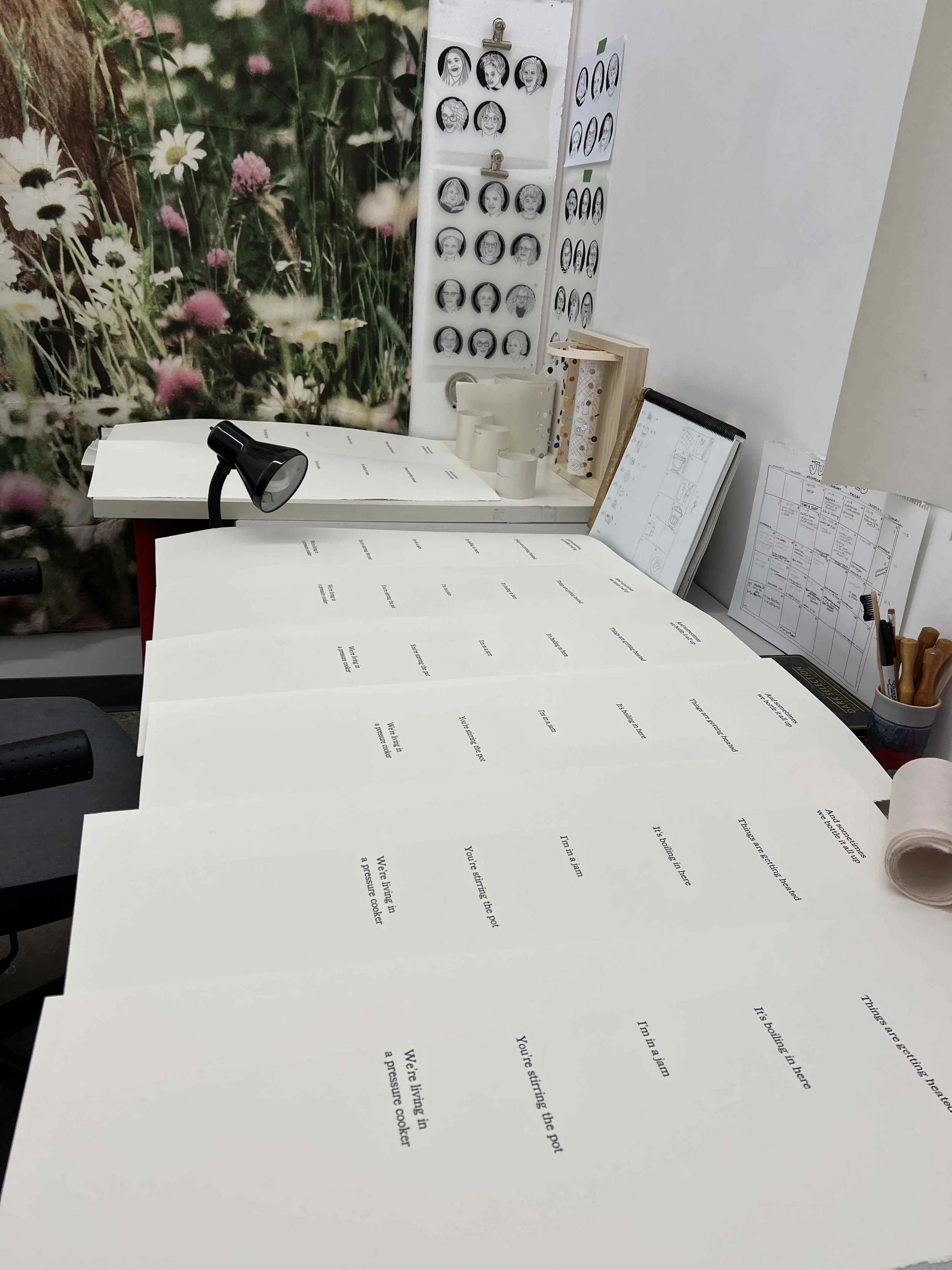 several semi-stacked sheets of paper with letter pressed phrases sit on a studio desk with circular portrait images in the background