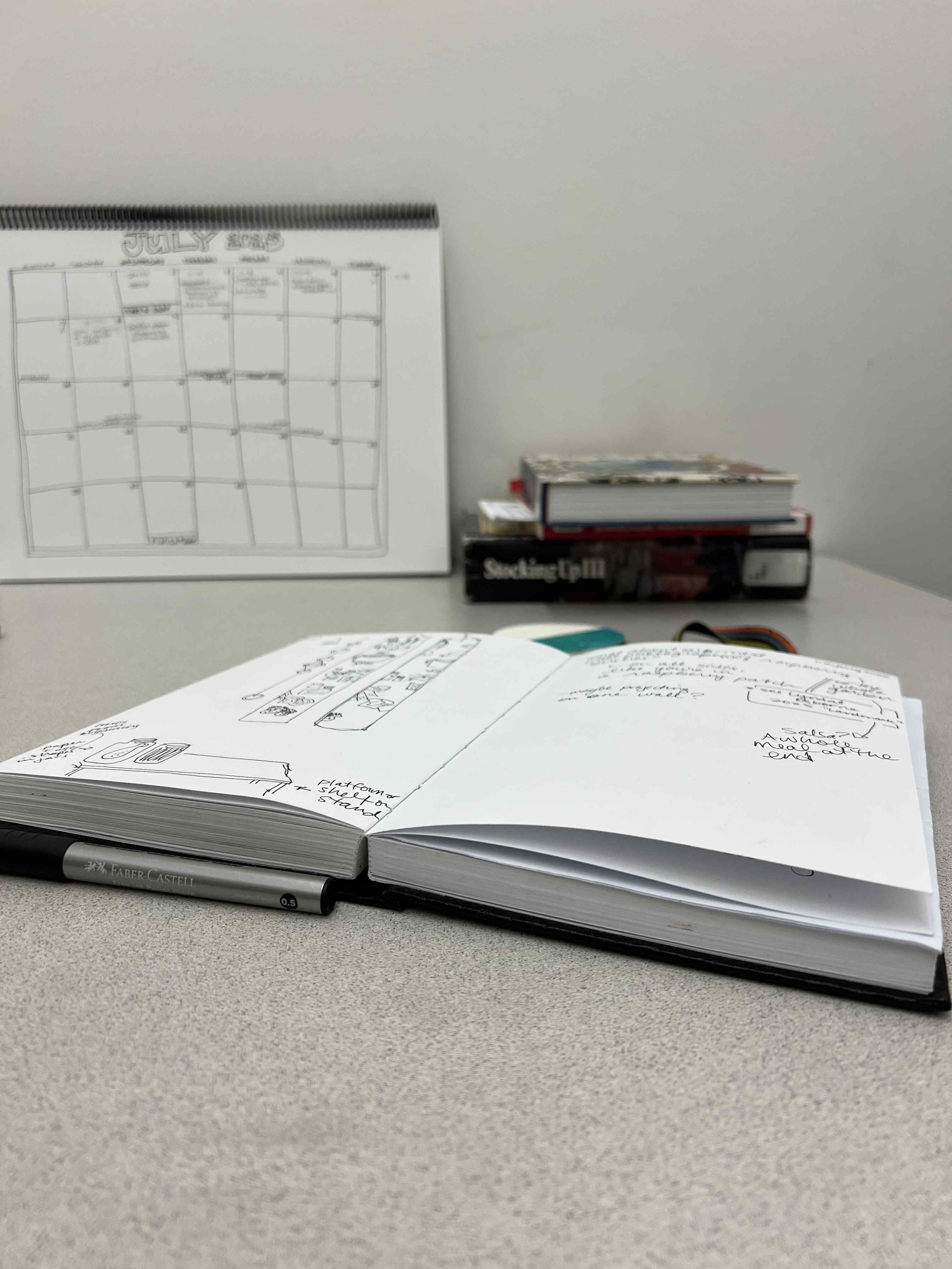 open sketchbook lies on desk in studio with books about home canning and a hand drawn calendar in the background