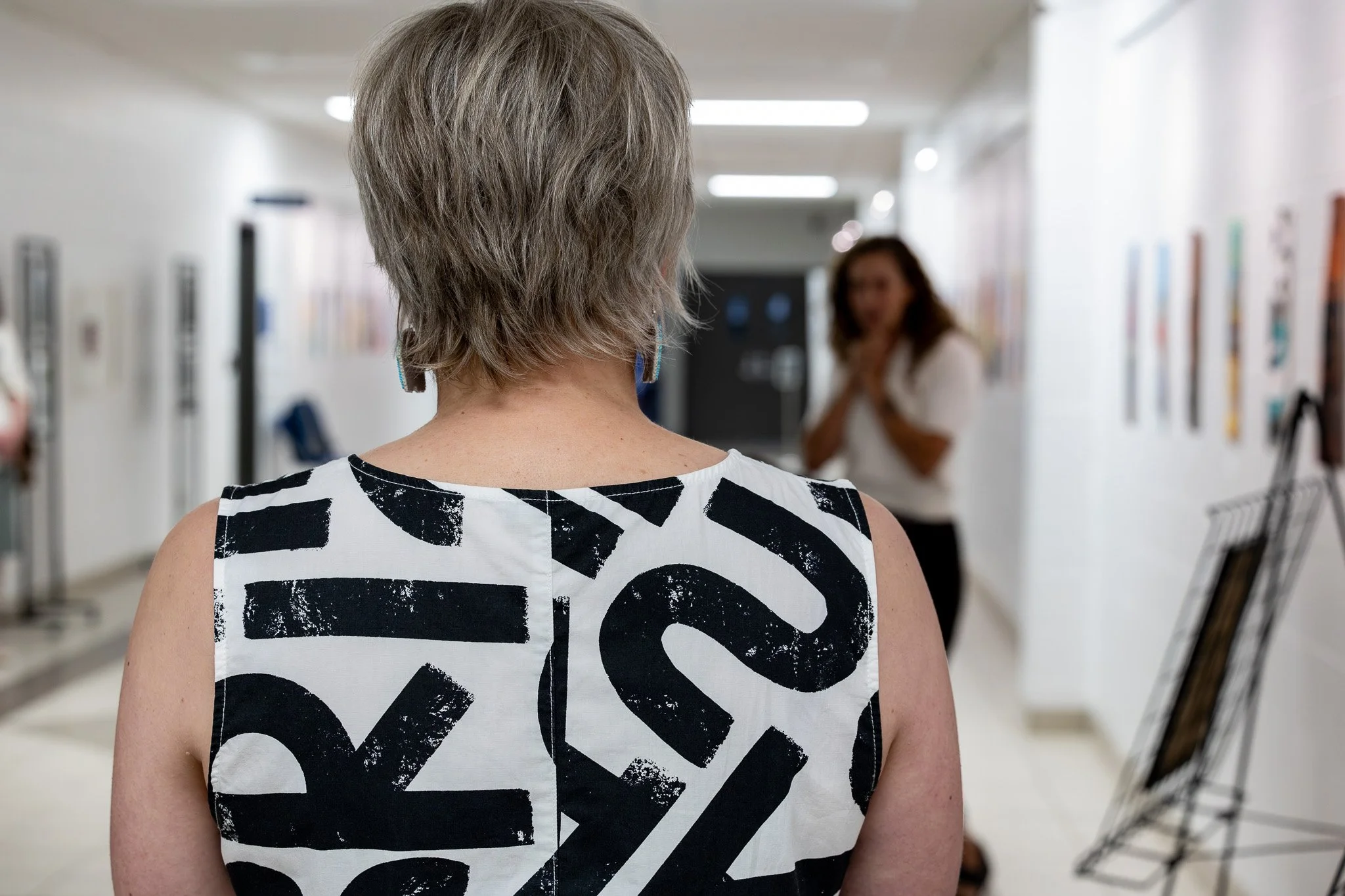 back of woman with short greyish hair and black and white dress in hallway with another woman