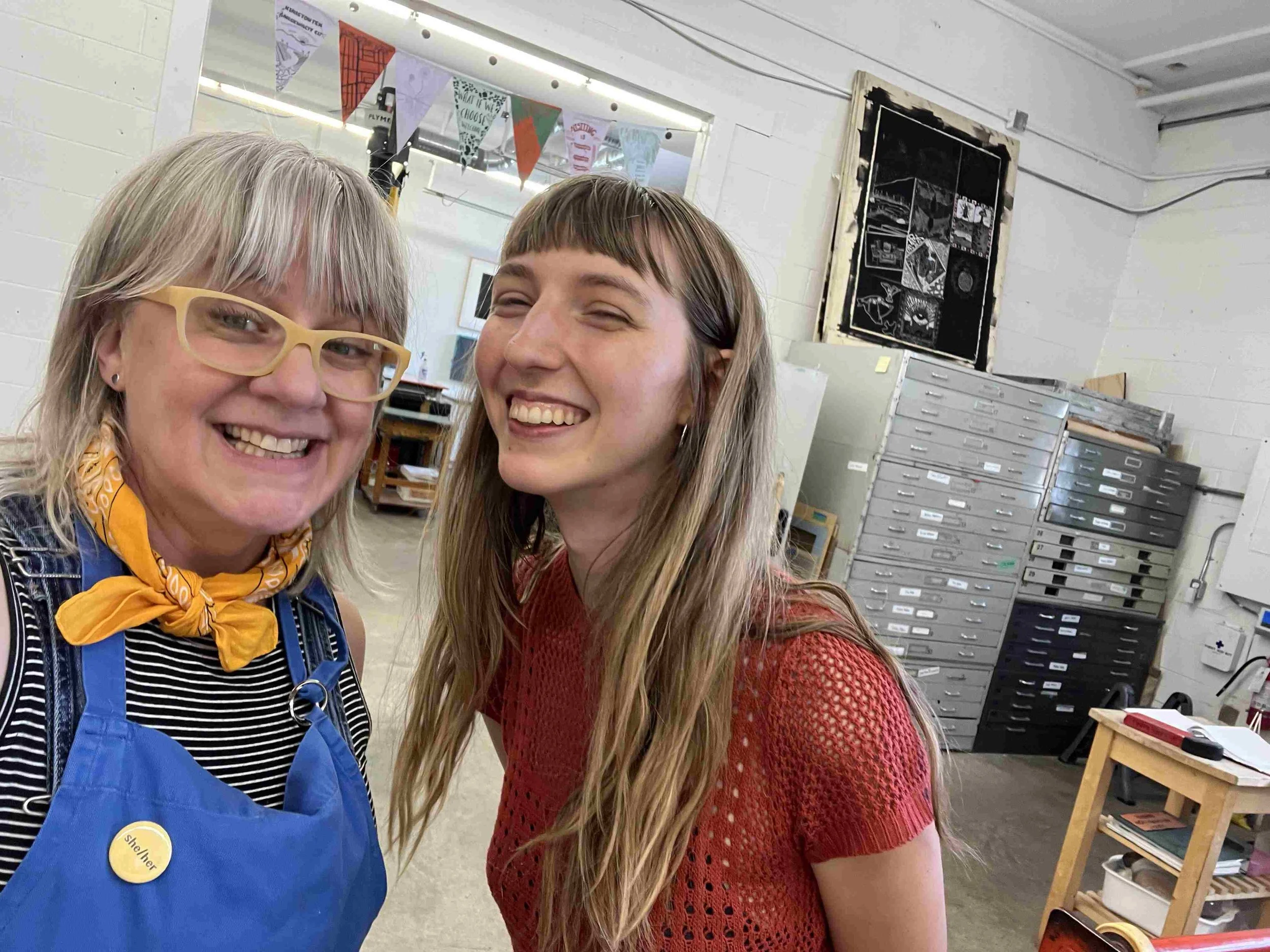 two white girls smile in front of flat lay file storage chests in print making workshop