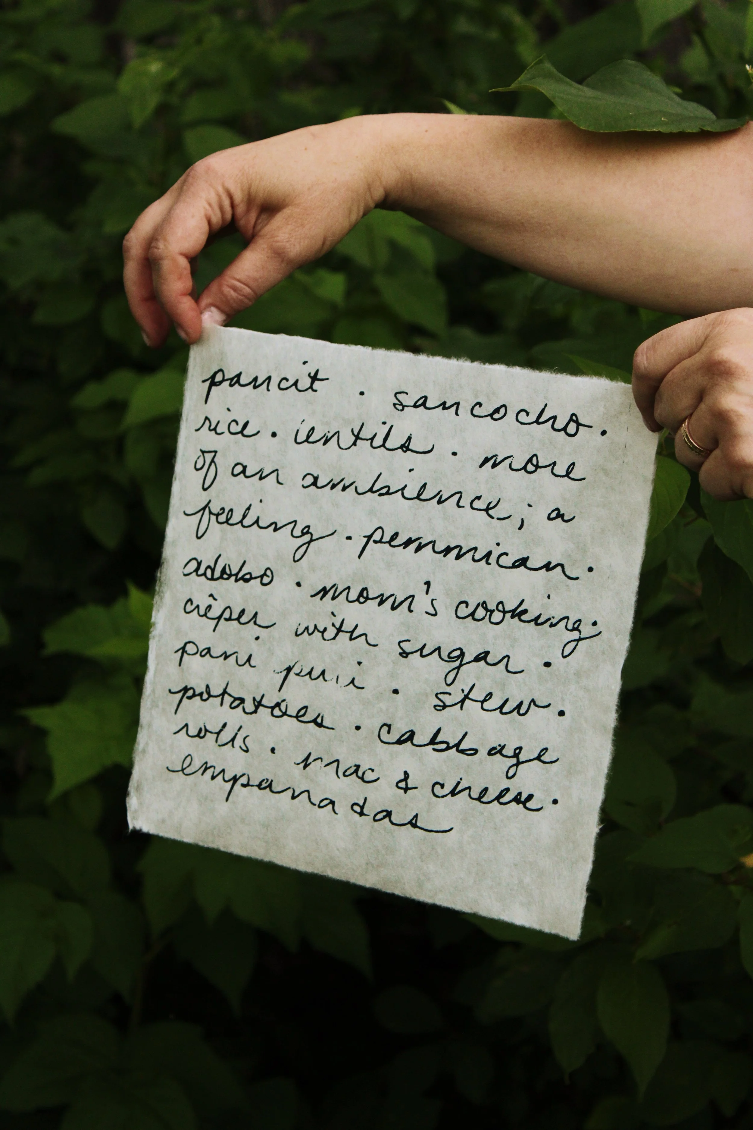 two pale-skinned hands hold paper with a list of community members' comfort foods in front of a leafy background