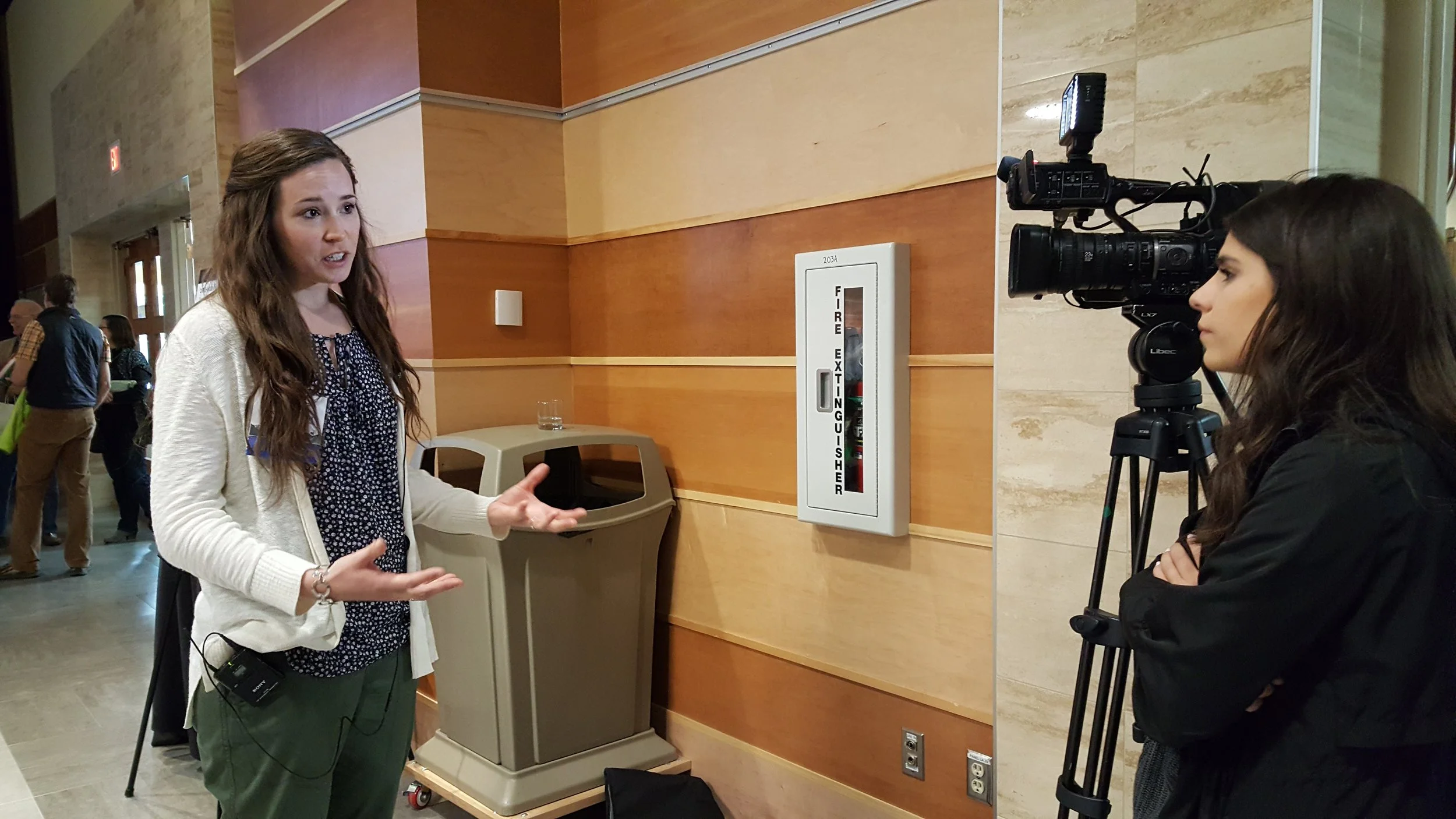 GYC's Special Projects Organizer Brooke Regan gives a recap of the symposium to a local news reporter on Tuesday. (Photo: GYC.)