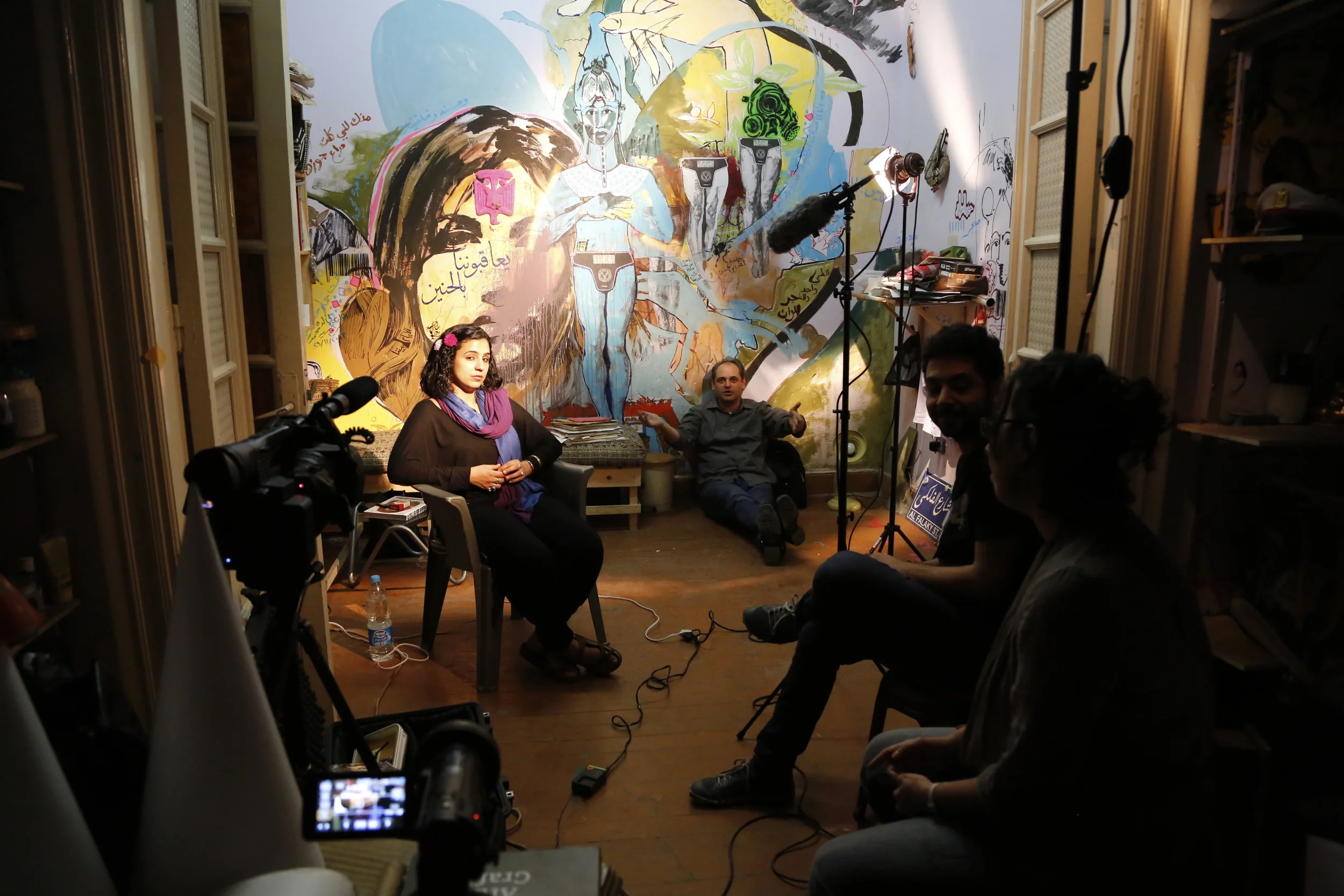  Director  Mark Nickolas  gesturing&nbsp;during a break in artist  Salma Samy's  interview. Artist  Ammar Abo Bakr  and co-director  Racha Najdi  on the right. 