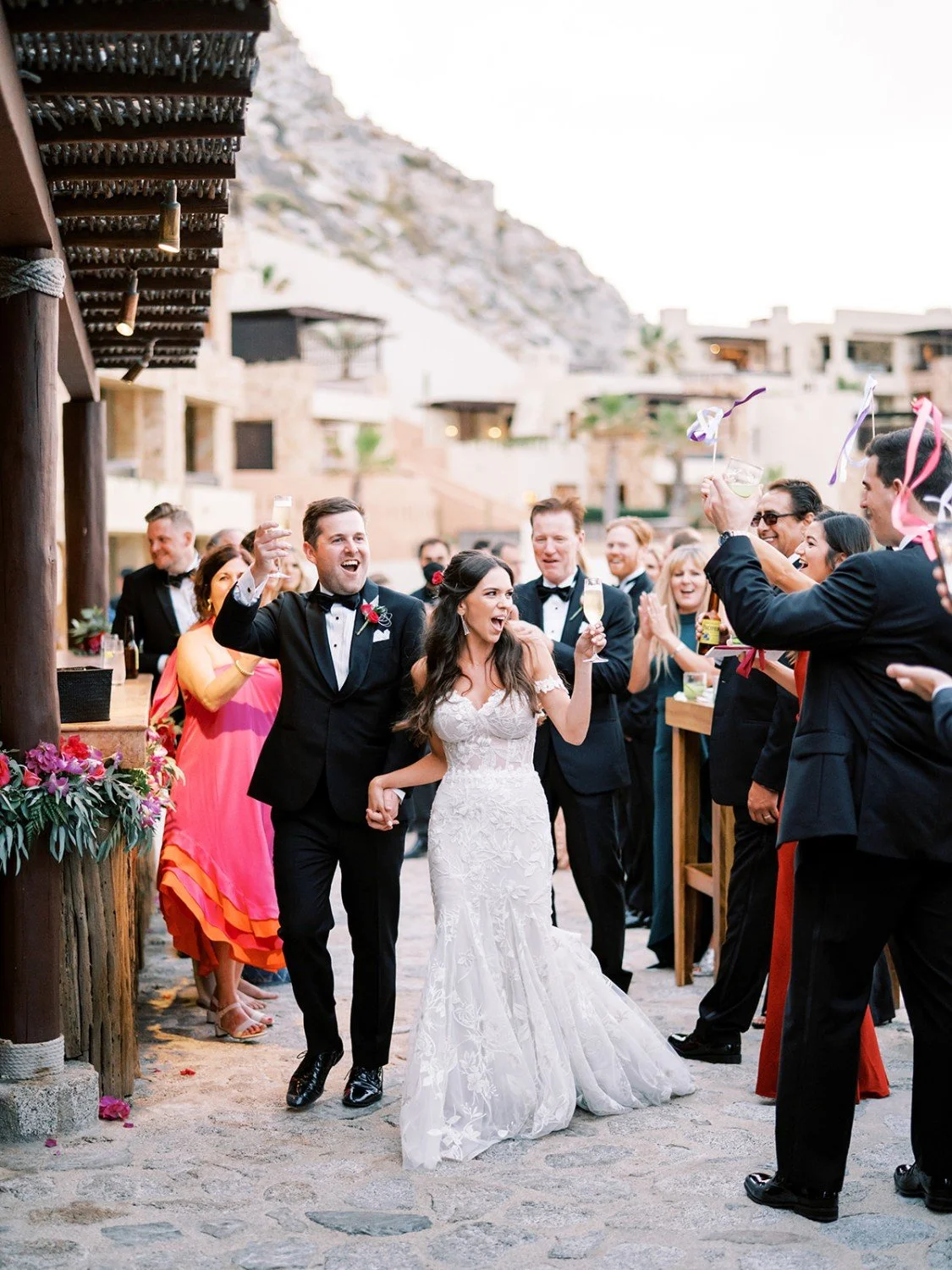 Bride and groom celebrating with wedding guests at an outdoor reception, with cocktails raised in the air.