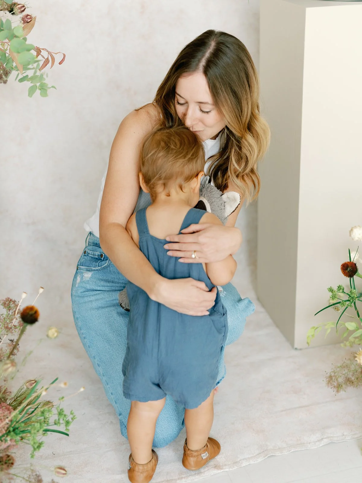 A woman is hugging a young child from behind in a cozy, softly lit room decorated with flowers.