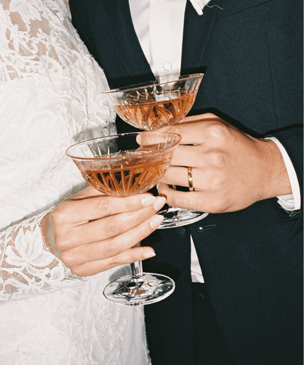 A bride and groom holding champagne flutes filled with a pink beverage during their wedding celebration.