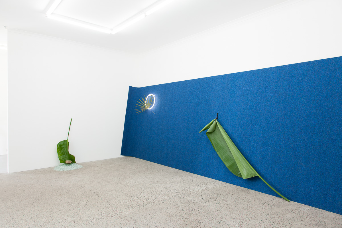 On the turning point of becoming and returning , 2016, Broken safety glass, rock, palm, carpet, neon, pressed palm, cock ring, Velcro, large palm, ipad, video from Blue Hawaii (1961), safety glass, rock, leaf. Photography: Docqument