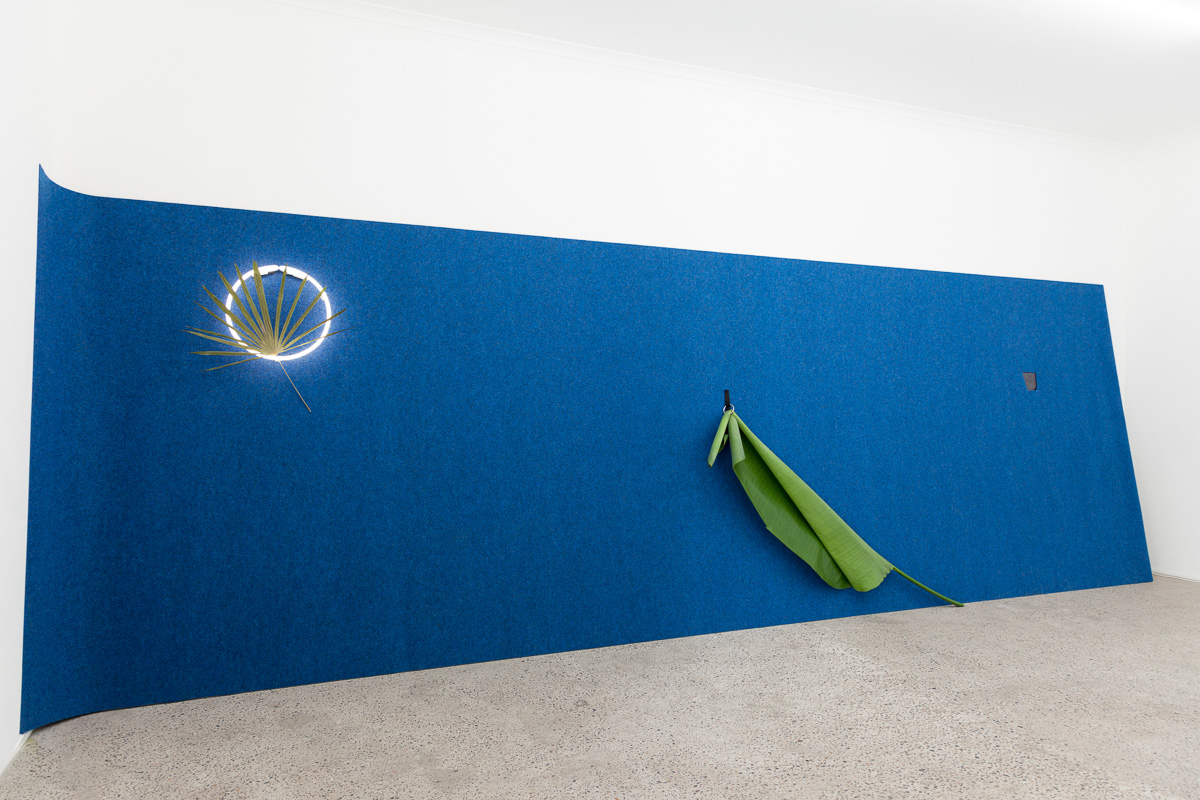 On the turning point of becoming and returning , 2016, Broken safety glass, rock, palm, carpet, neon, pressed palm, cock ring, Velcro, large palm, ipad, video from Blue Hawaii (1961), safety glass, rock, leaf. Photography: Docqument