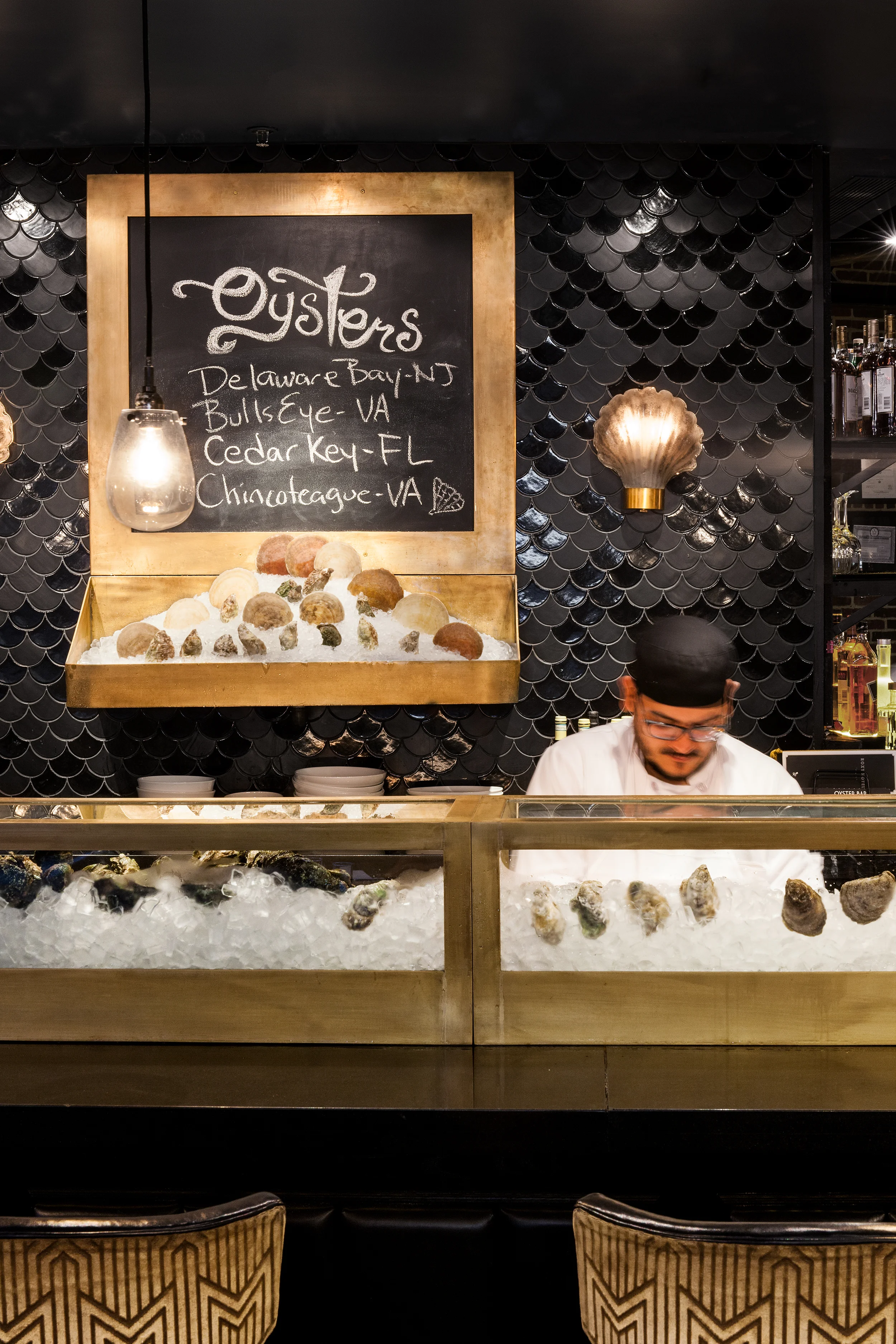 ROXY OYSTER BAR and CONCESSION New York, NY The Roxy Hotel in TriBeCa hired us to help realize a radical transformation of their public amenity spaces within the hotel. STUDIOjamieson took several under-utilized spaces and transformed them into branded programming within the hotel. We first inserted Jack's Stir Brew Coffee into a former egress bay of the facade. We were then commissioned to create a new Oyster Bar within the existing lobby restaurant area and a new concession stand to service their basement art-house cinema. The Oyster Bar features custom brushed brass cold display cases, vintage clam-shell lighting sconces and Moroccan fish-scales mosaic tile. The Concession stand features a custom curved wood and glass display case to compliment the existing cinema lobby geometry. The neon cinema sign was salvaged and retrofit to serve as the new menu board. Theater style lighting was added to complete the look. All photography © Heidi's Bridge