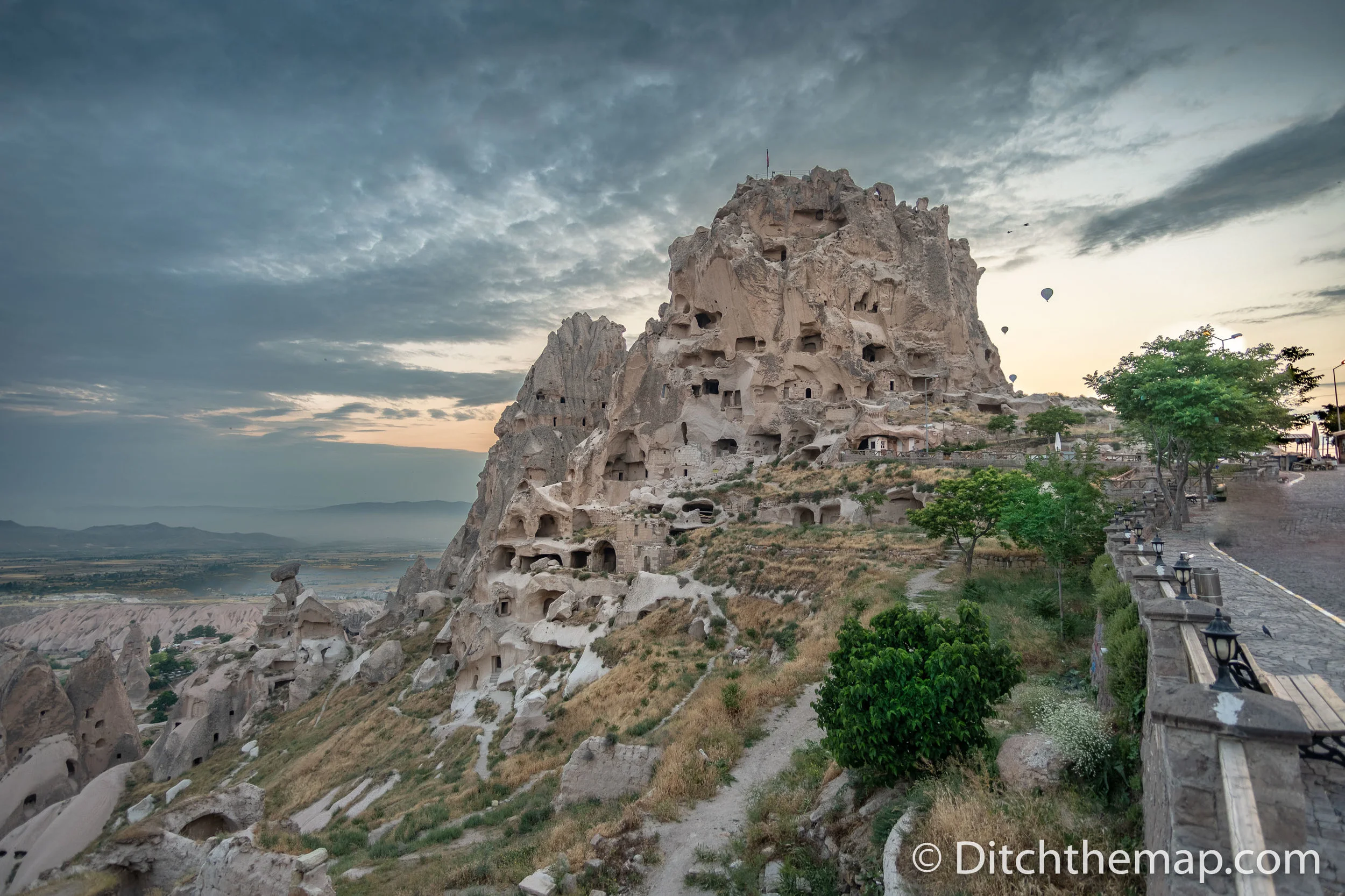 Uchisar Castle in Cappadocia, Turkey with balloons in background