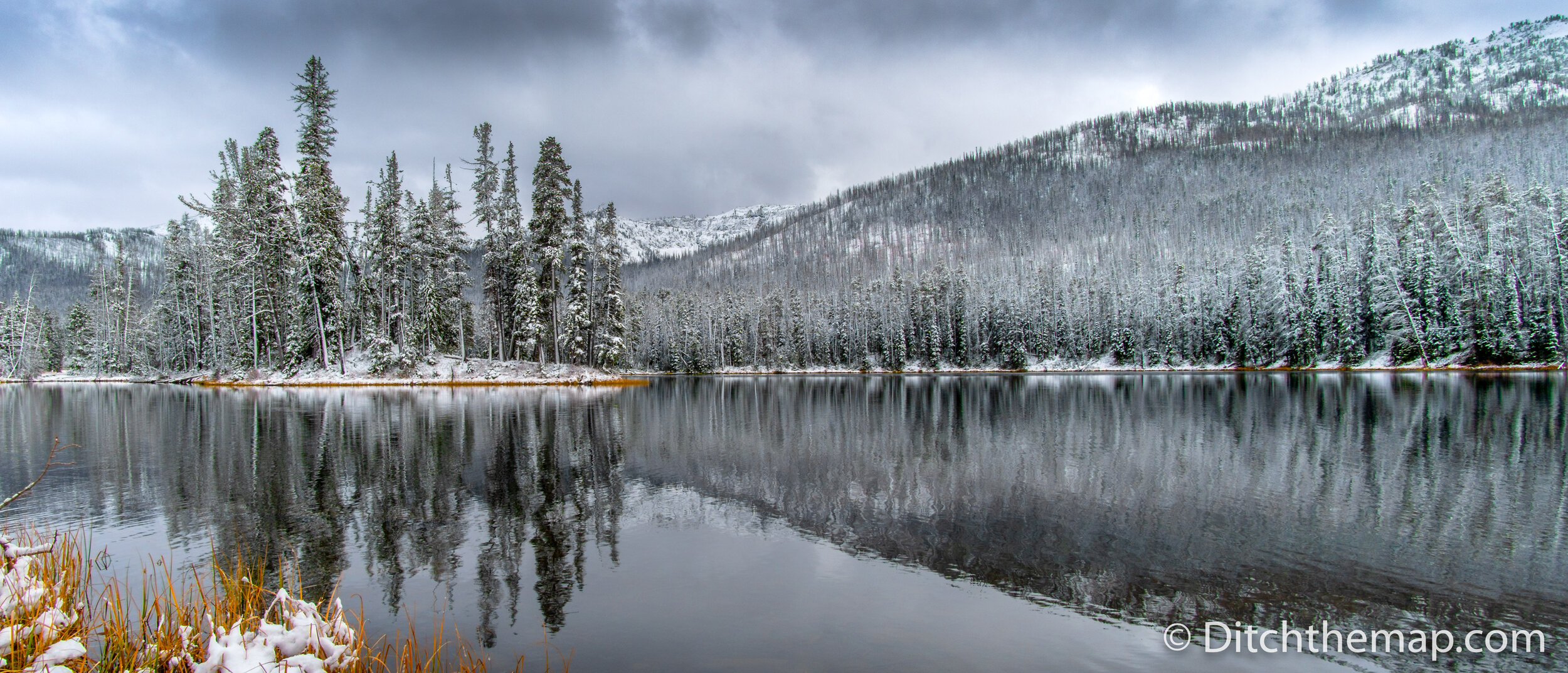 Light snow covered trees and mountain with reflection on lake