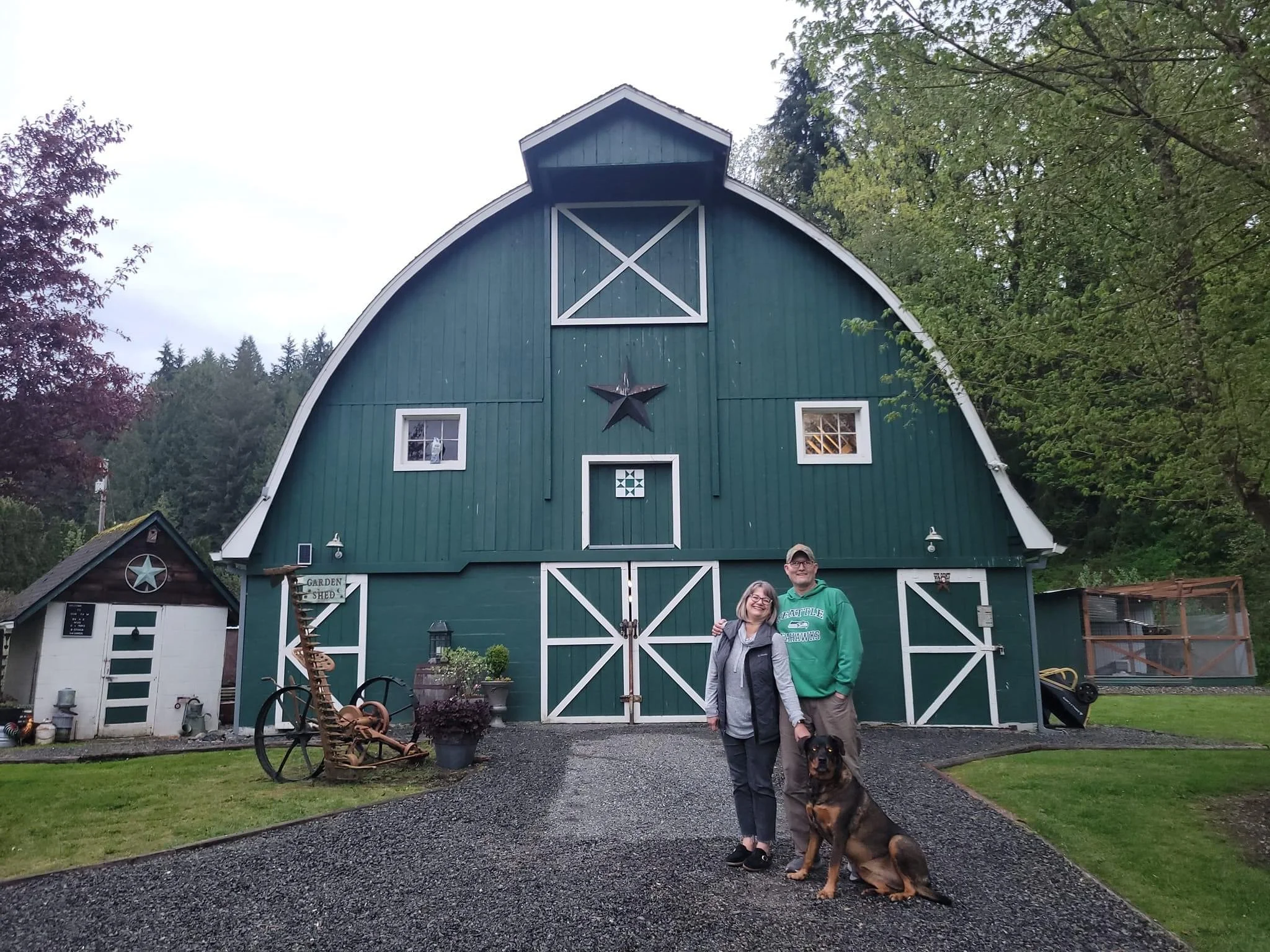 Carrie O'Keefe and her husband stand in front of their barn with their dog.
