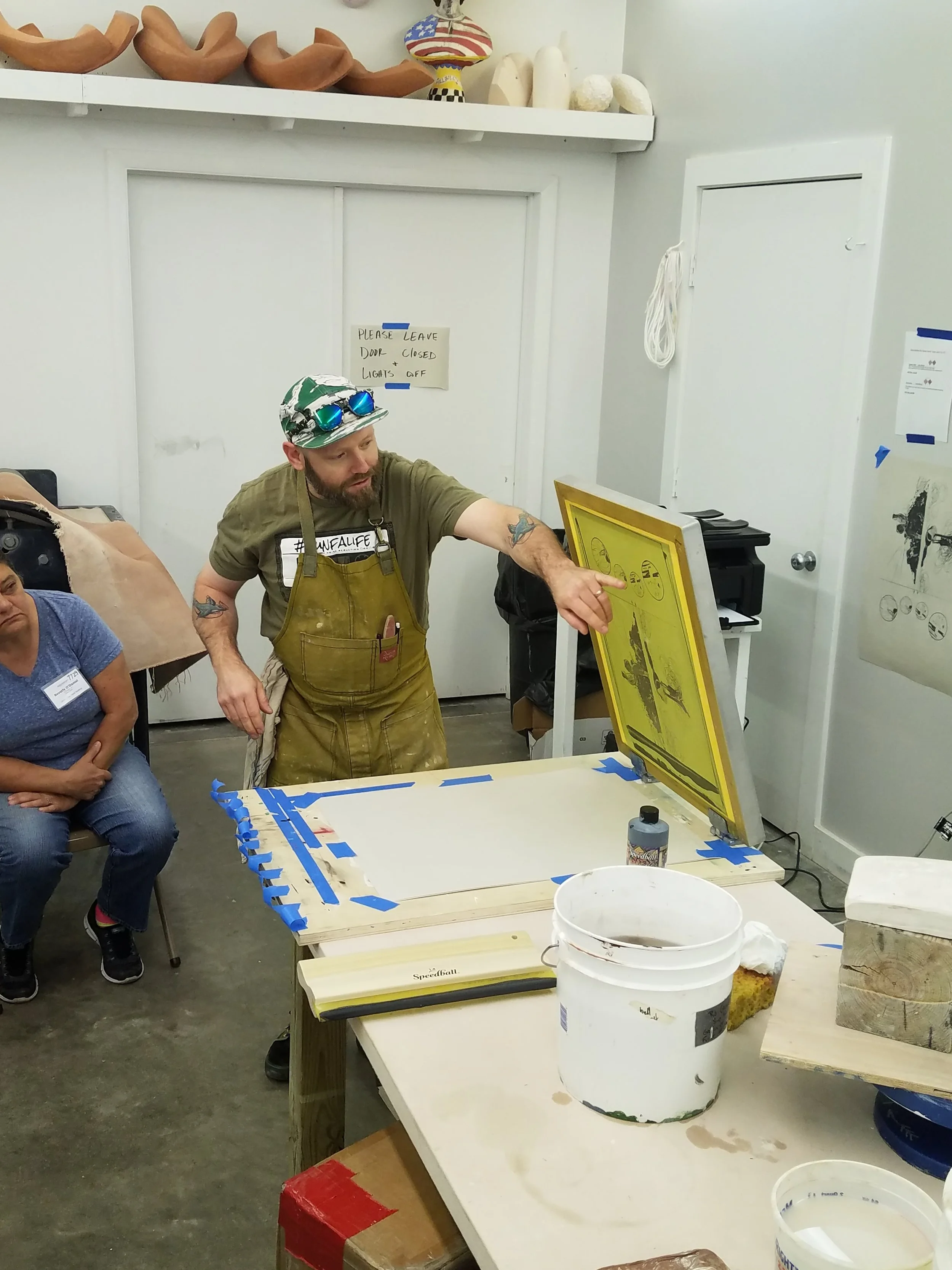 Israel is giving a demo on how to screen print onto newsprint with underglaze for a newprint transfer.