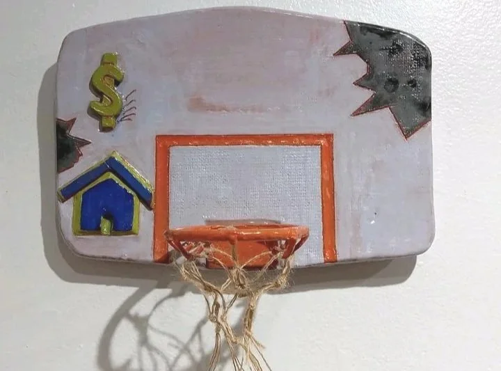 Decorative miniature basketball hoop with colorful decorations of a dollar sign, a house, and a black and red star on a wall.