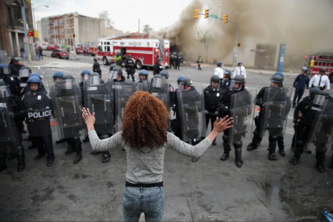 A woman faces down a line of Baltimore police officers in riot gear on Monday during protests after the funeral of Freddie Gray. Courtesy of The Washington Post.