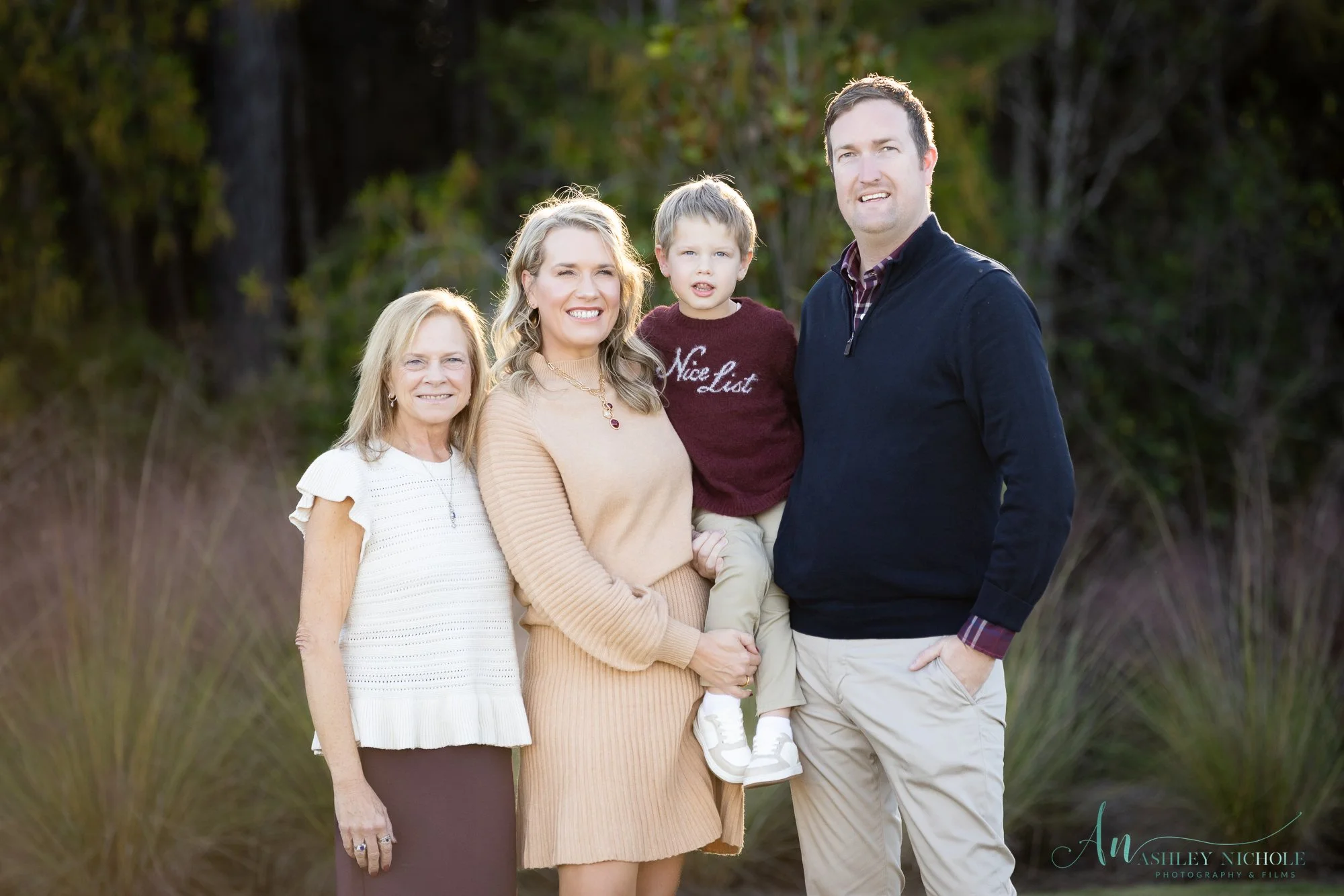 Family portrait of four people outdoors with trees in background
