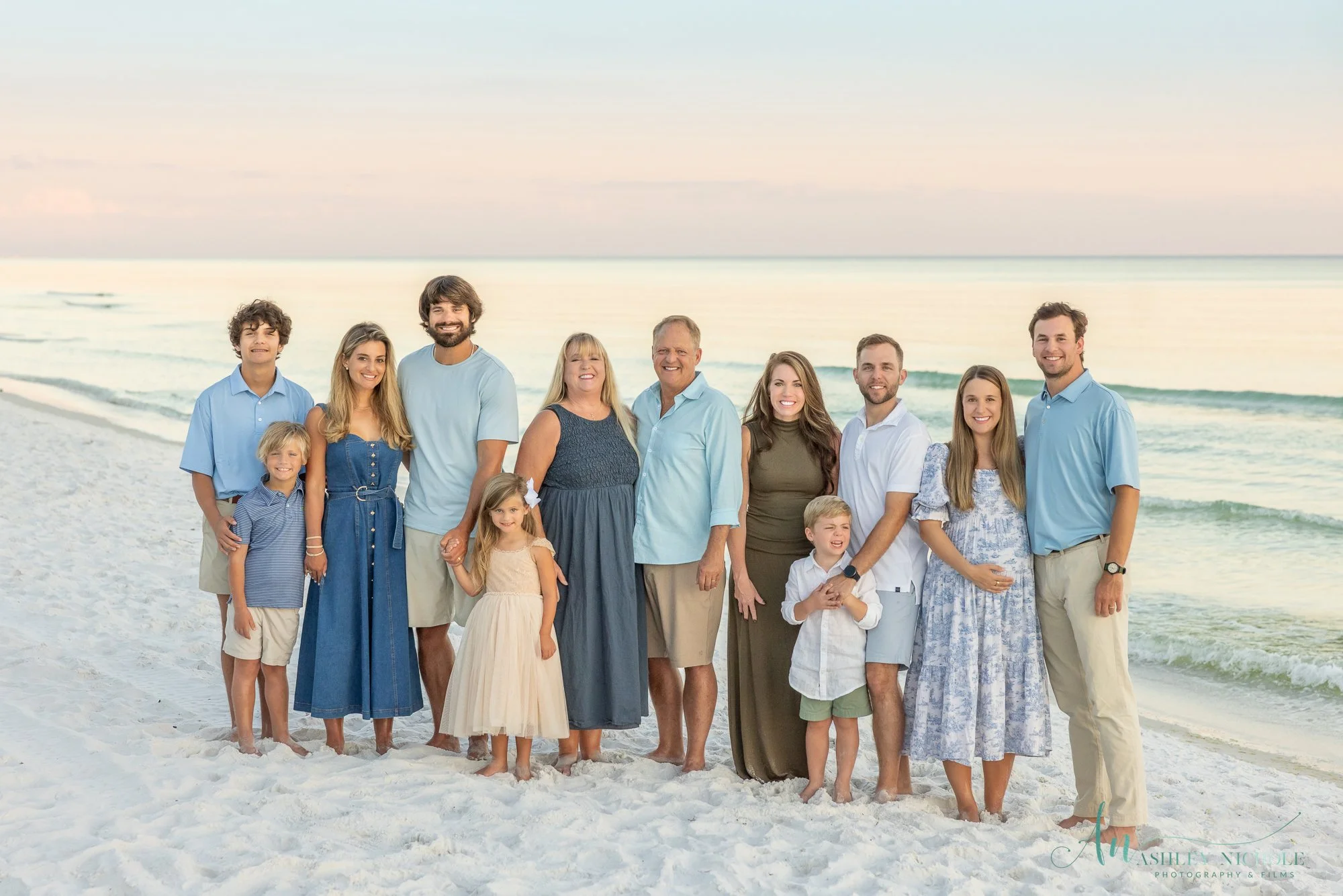 Family group standing on a beach, smiling, with ocean waves in the background during sunset.