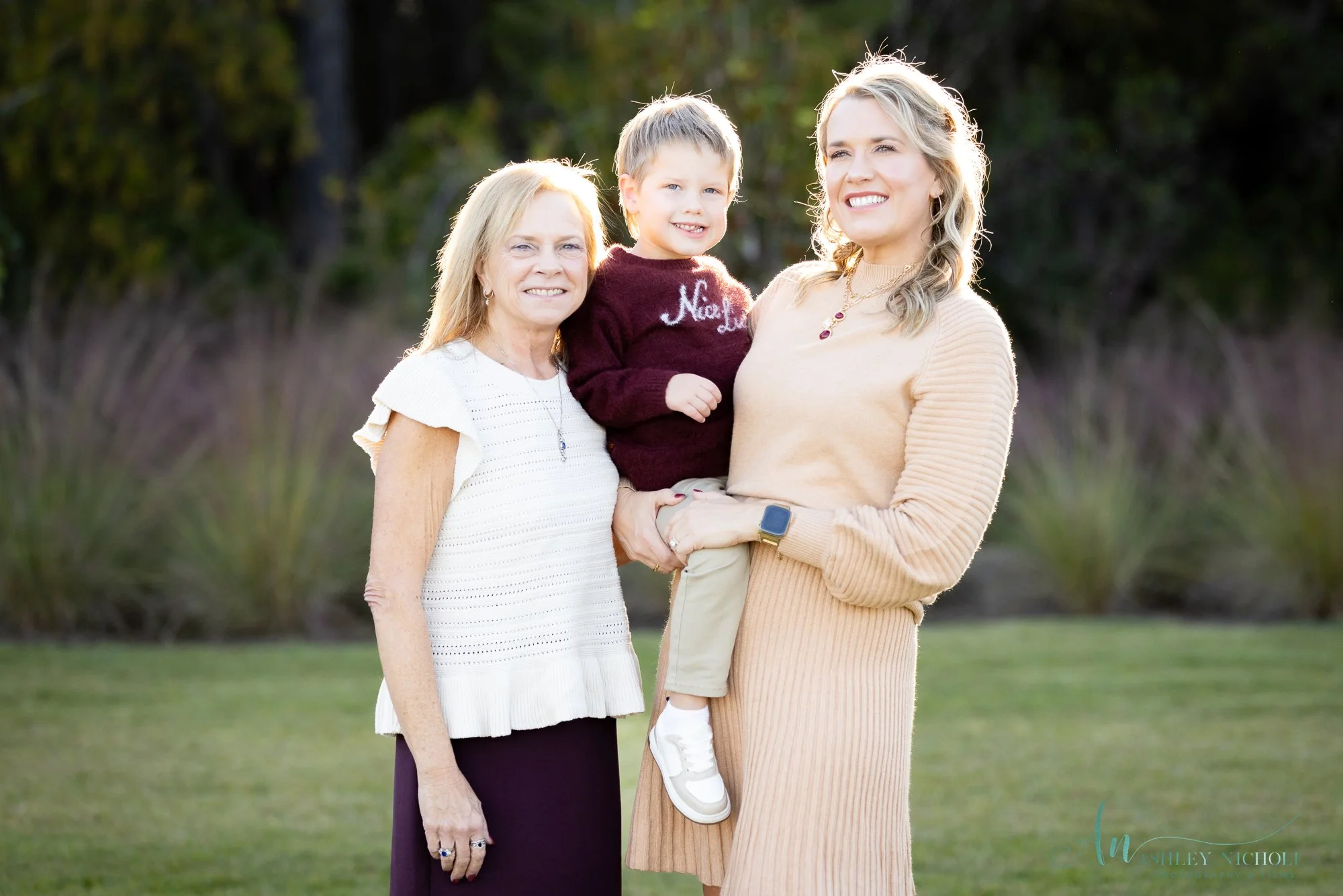 Three women and a young boy outdoors, smiling, with trees and grass in the background.