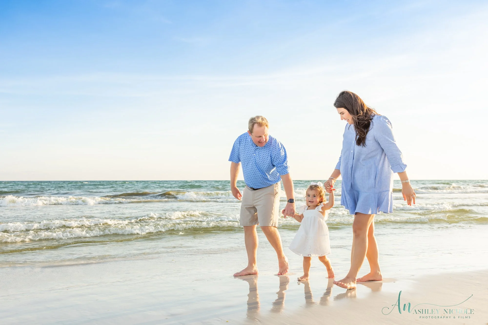 A family of three, two adults and a young girl, enjoying time together on the beach near the ocean.