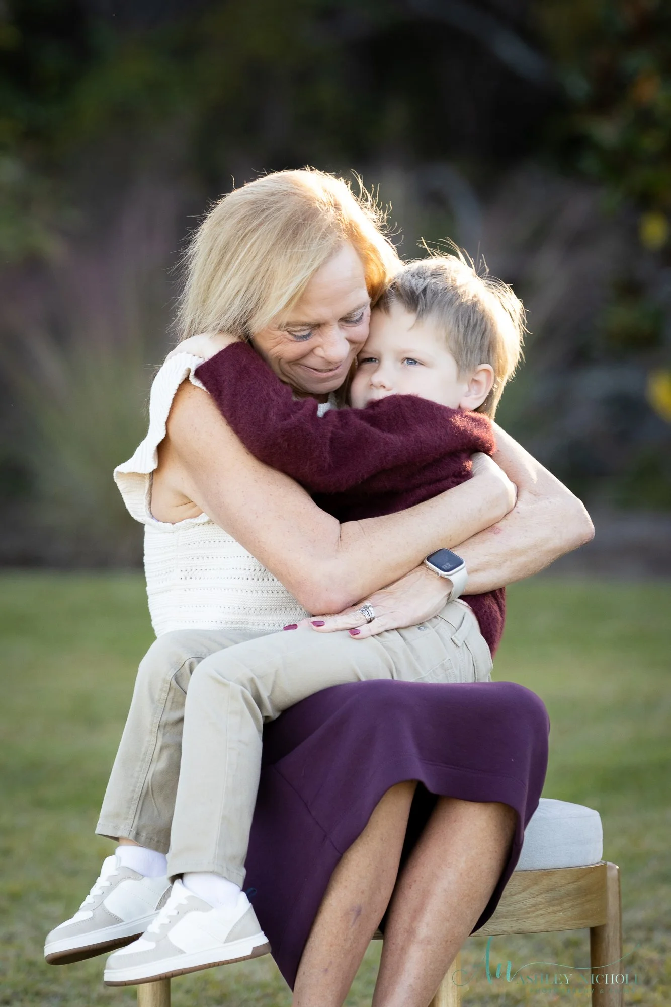 A woman with short blonde hair hugging a young boy outdoors in a park.