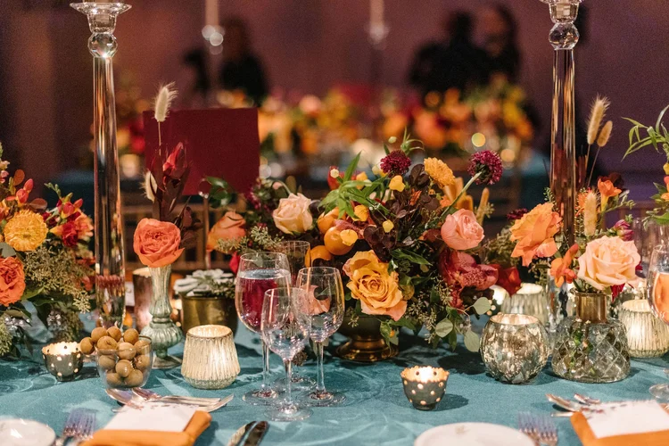 Orange roses and autumn blooms with candles on a teal tablecloth