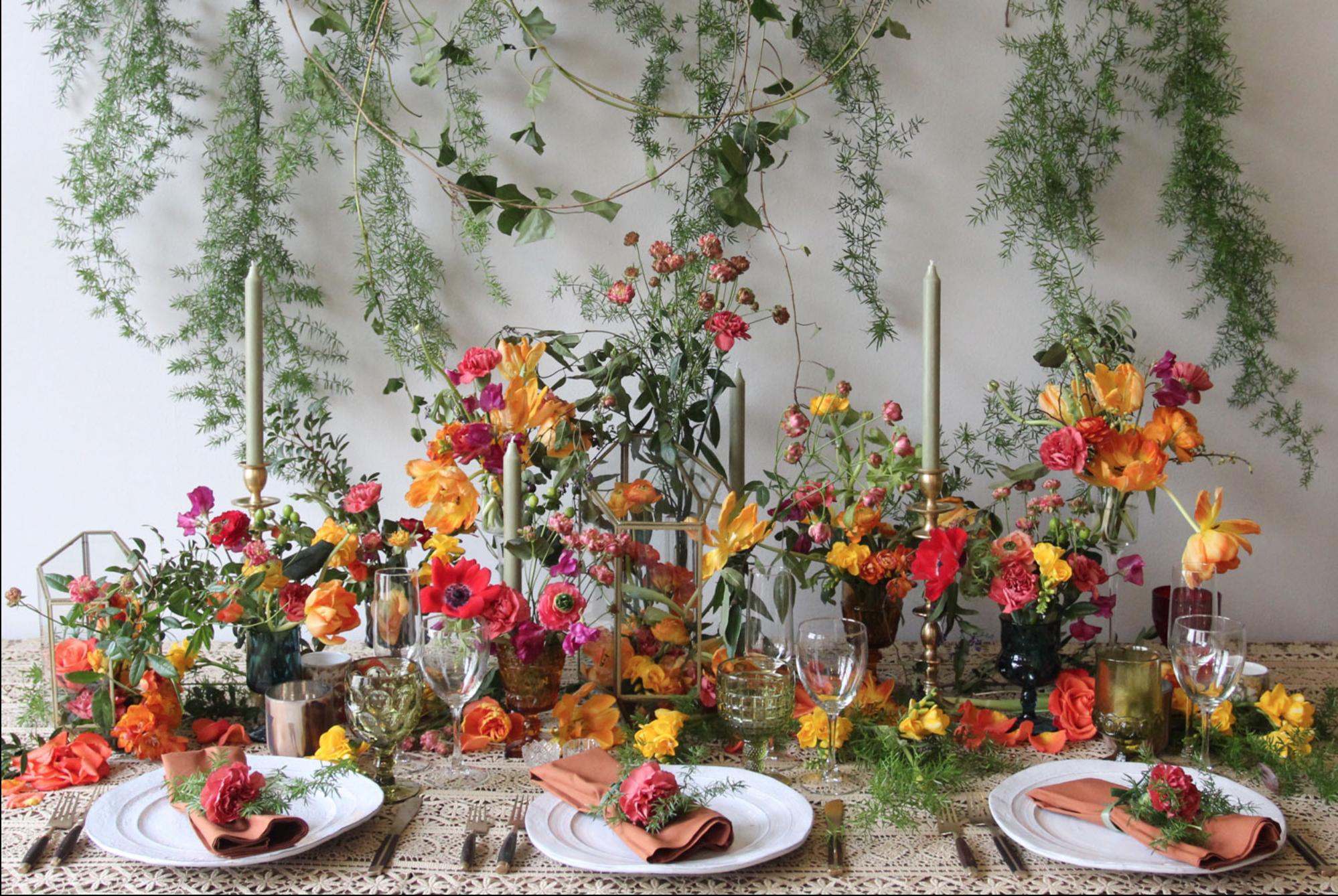 Hanging greenery above a dinner table crowded with red, orange and pink flowers