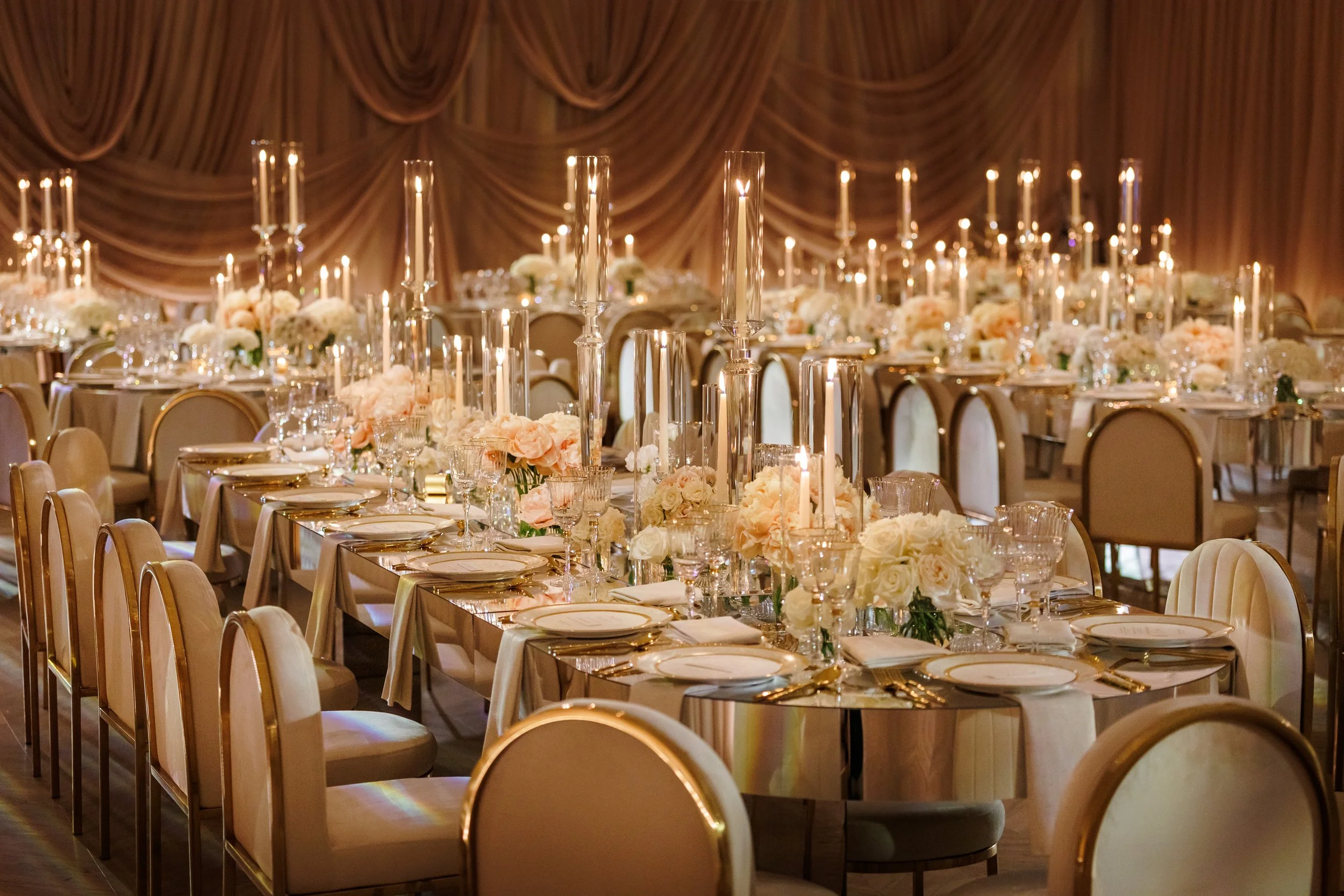 A ballroom reception with tall gold candelabras and low blush arrangements