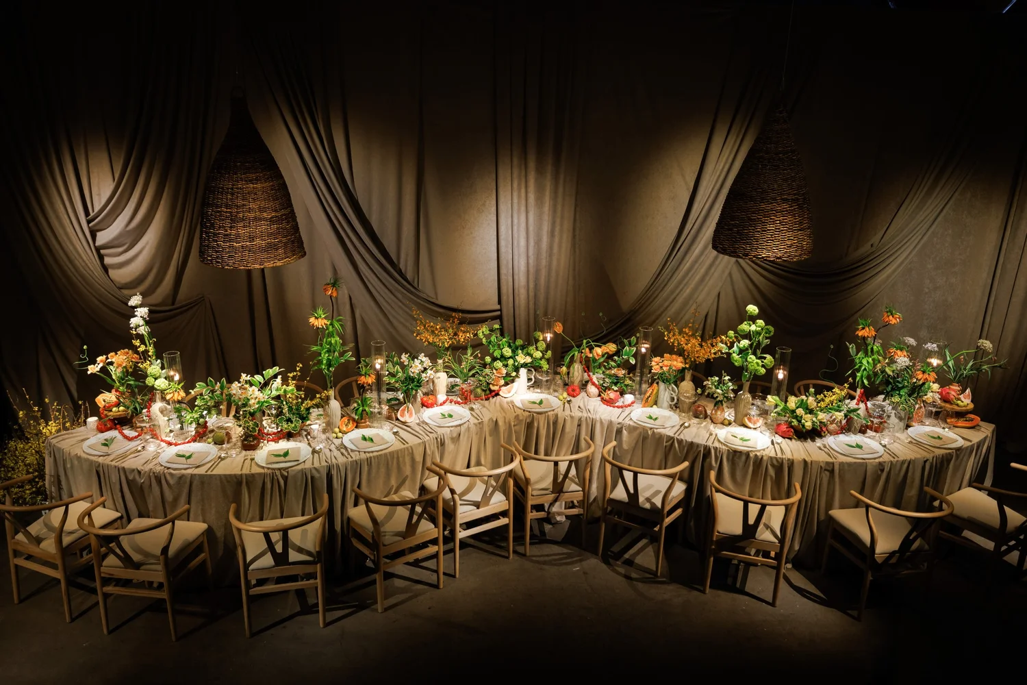 A long table through a draped room, covered in low garden flowers and candles