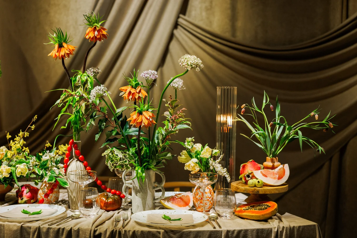A low-lit tablescape of orange blooms and wild stems in glass vessels
