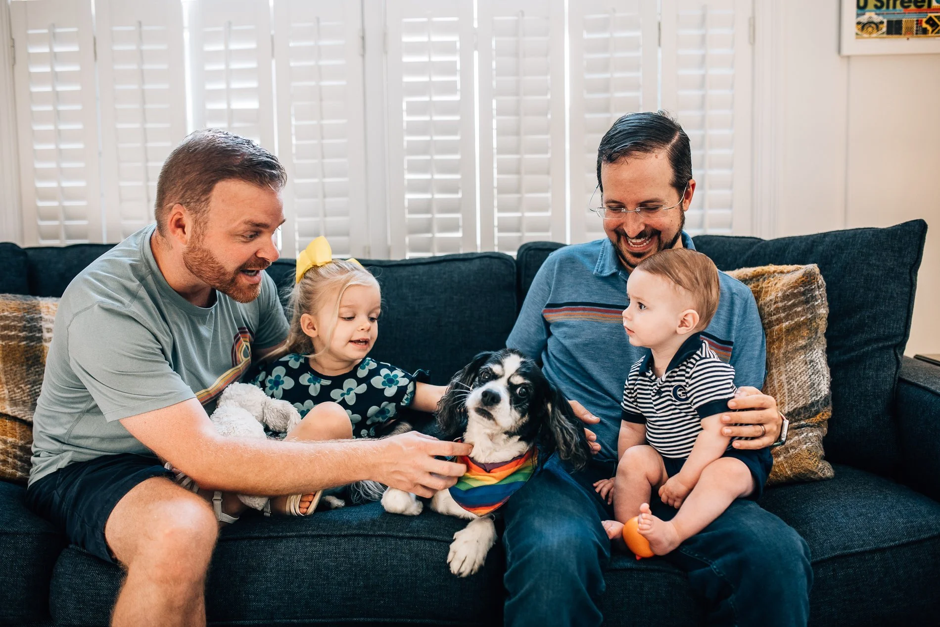 2 dads and 2 young kids on the sofa with their dog