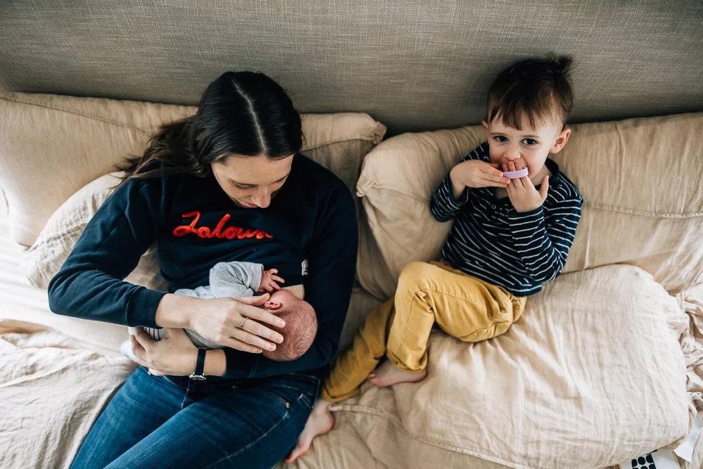mother on the bed looking down at her newborn baby with toddler by her side