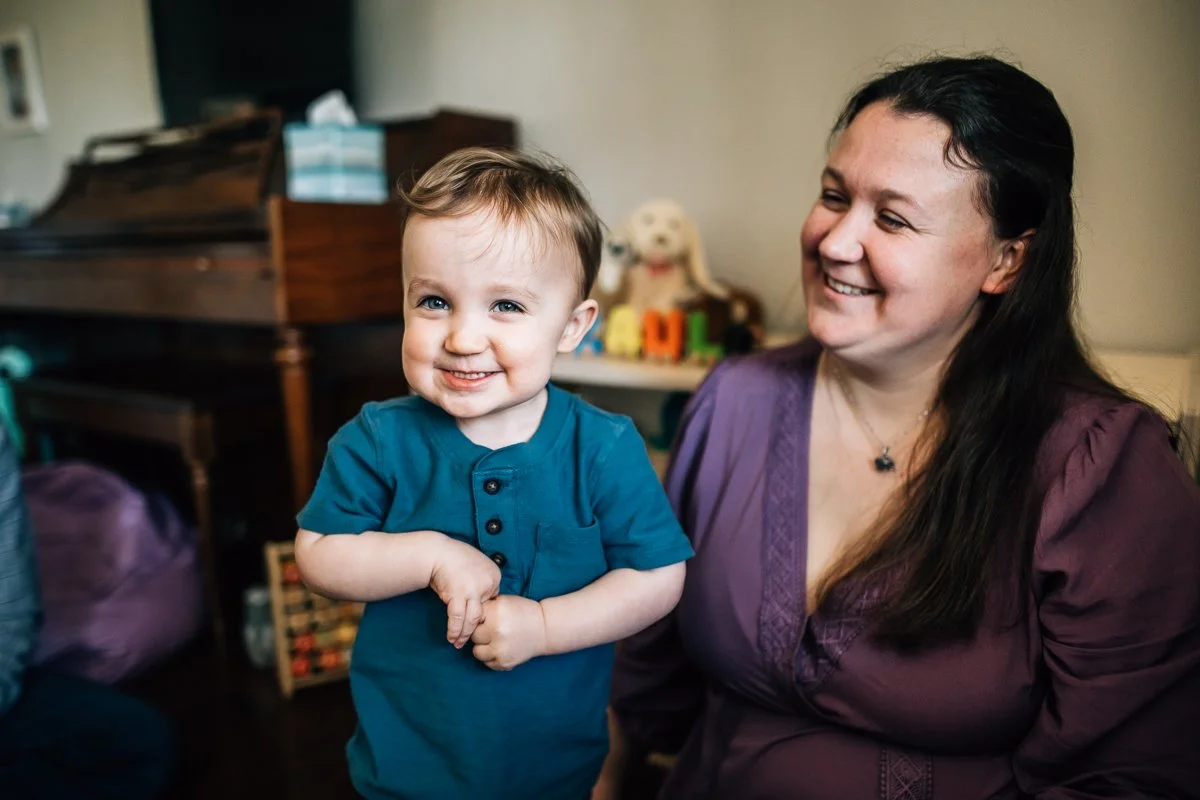 toddler smiling at the camera while mom is looking at him