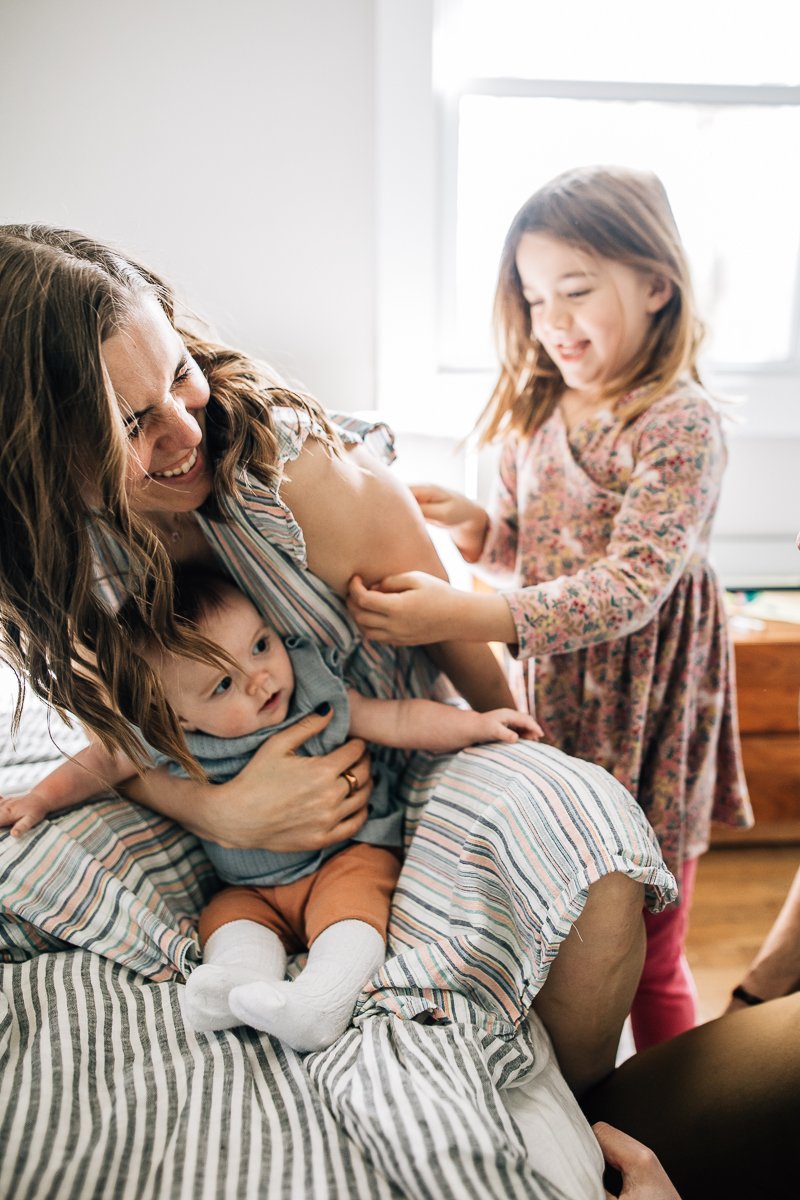 little girl tickling her mom holding a newborn