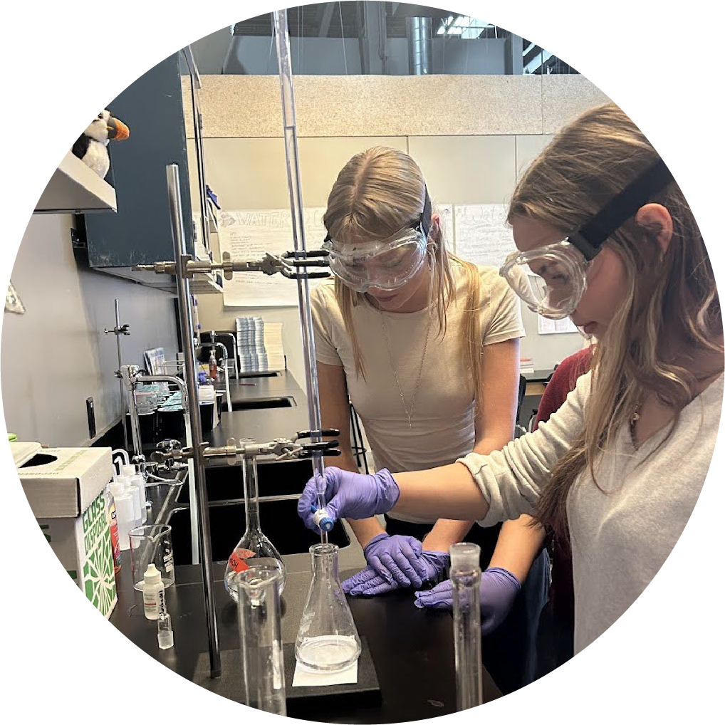 Two Watershed students in safety goggles running a chemistry experiment