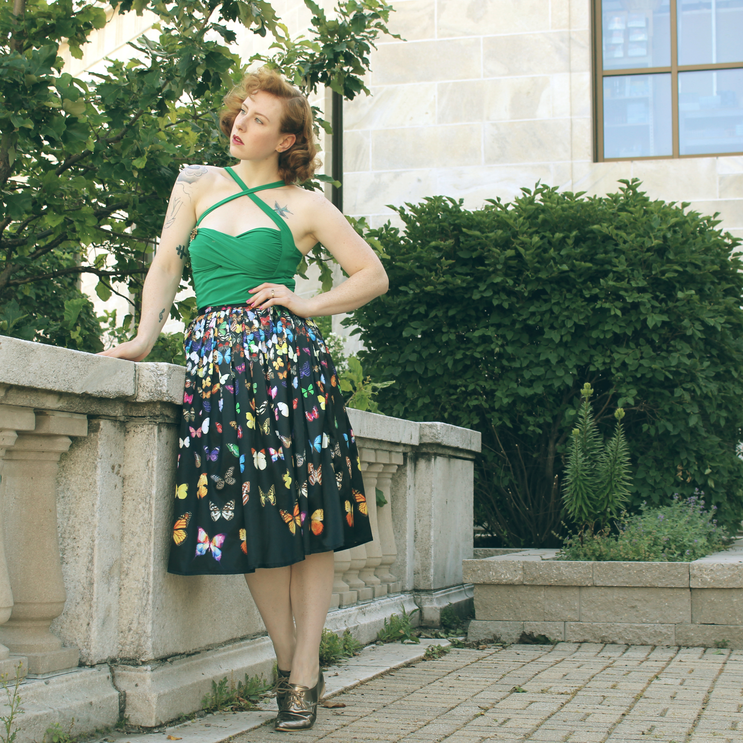 Zella Maybe in a butterfly print skirt with a green top and gold shoes. At the Shedd Aquarium looking out over Chicago. Vintage fashion blogger.